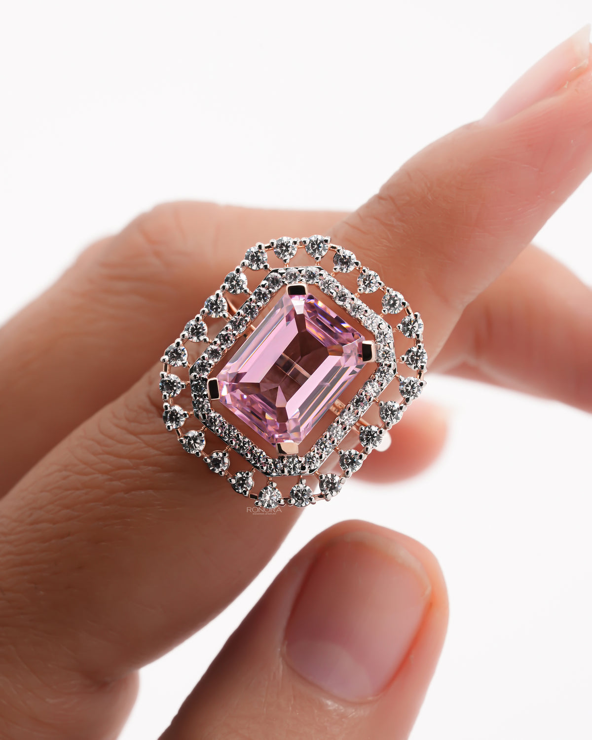 Close-up of a pink emerald cut double halo ring in rose gold on a finger, surrounded by white stone halos