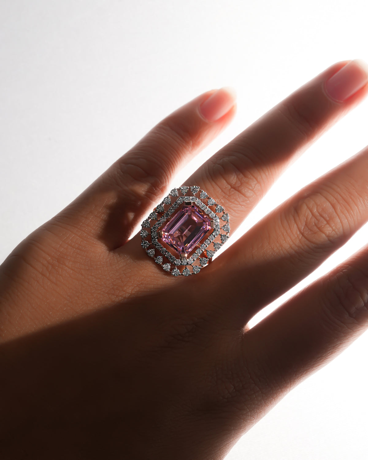 Pink emerald cut double halo ring in rose gold worn on a hand, large pink centre stone and white stone halos