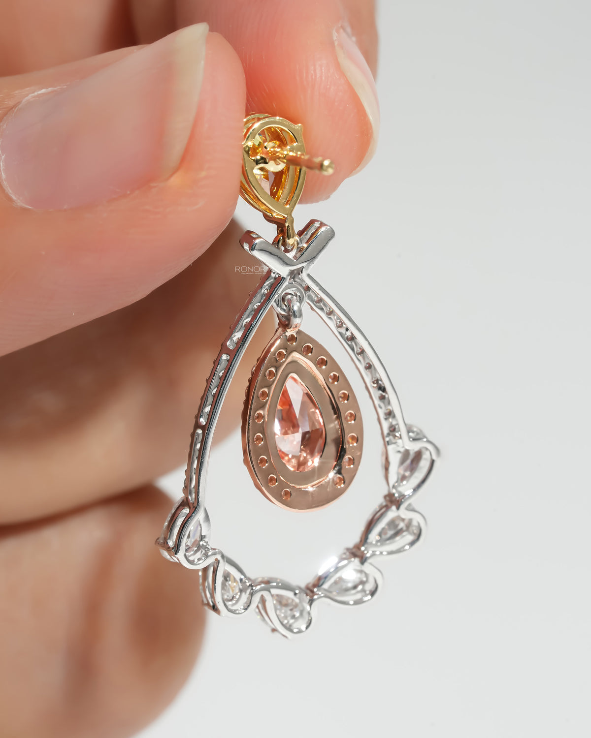 Back of pink pear lab grown diamond drop earrings held in fingers, showing rose gold halo and pear diamond frame