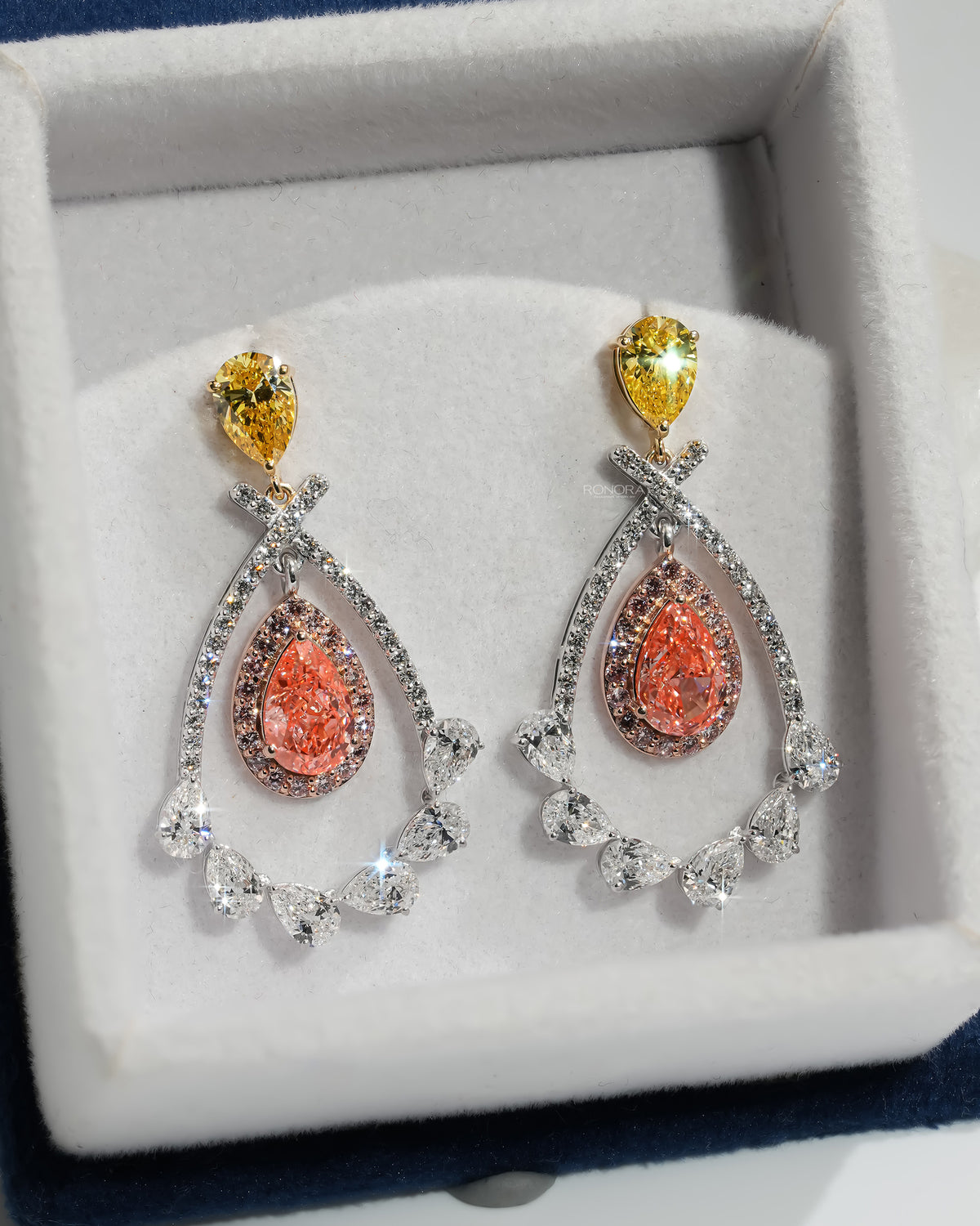 Pink pear lab grown diamond drop earrings with yellow pear tops in a white velvet jewelry box, top angle view