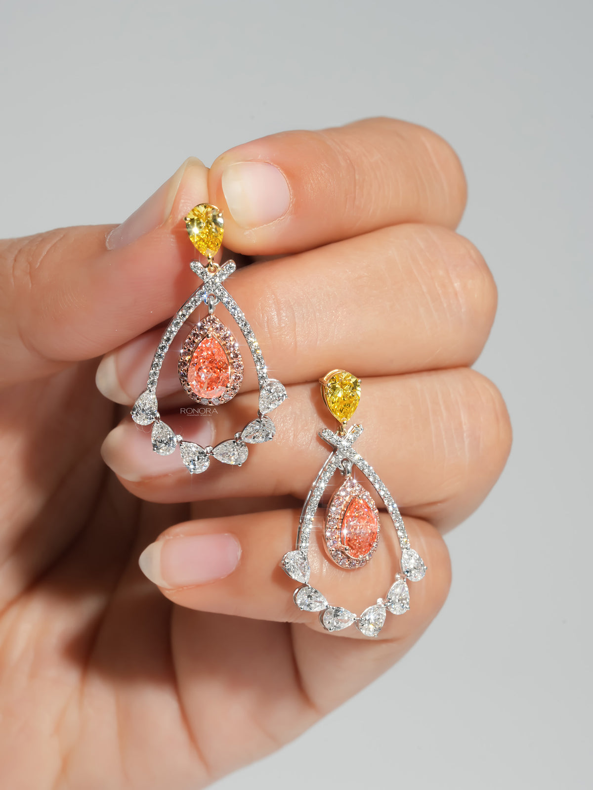 Pink pear lab grown diamond drop earrings with yellow pear tops held on fingertips, white pear diamond teardrop frame