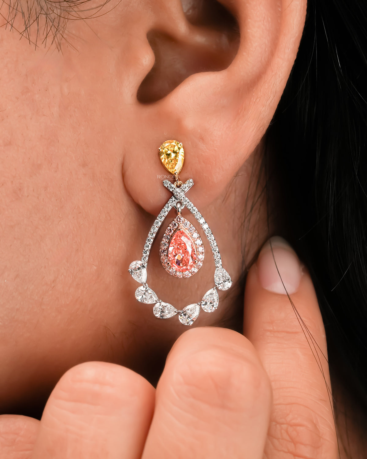 Close-up of an ear wearing a pink pear lab grown diamond drop earring with a yellow pear top and white diamond frame