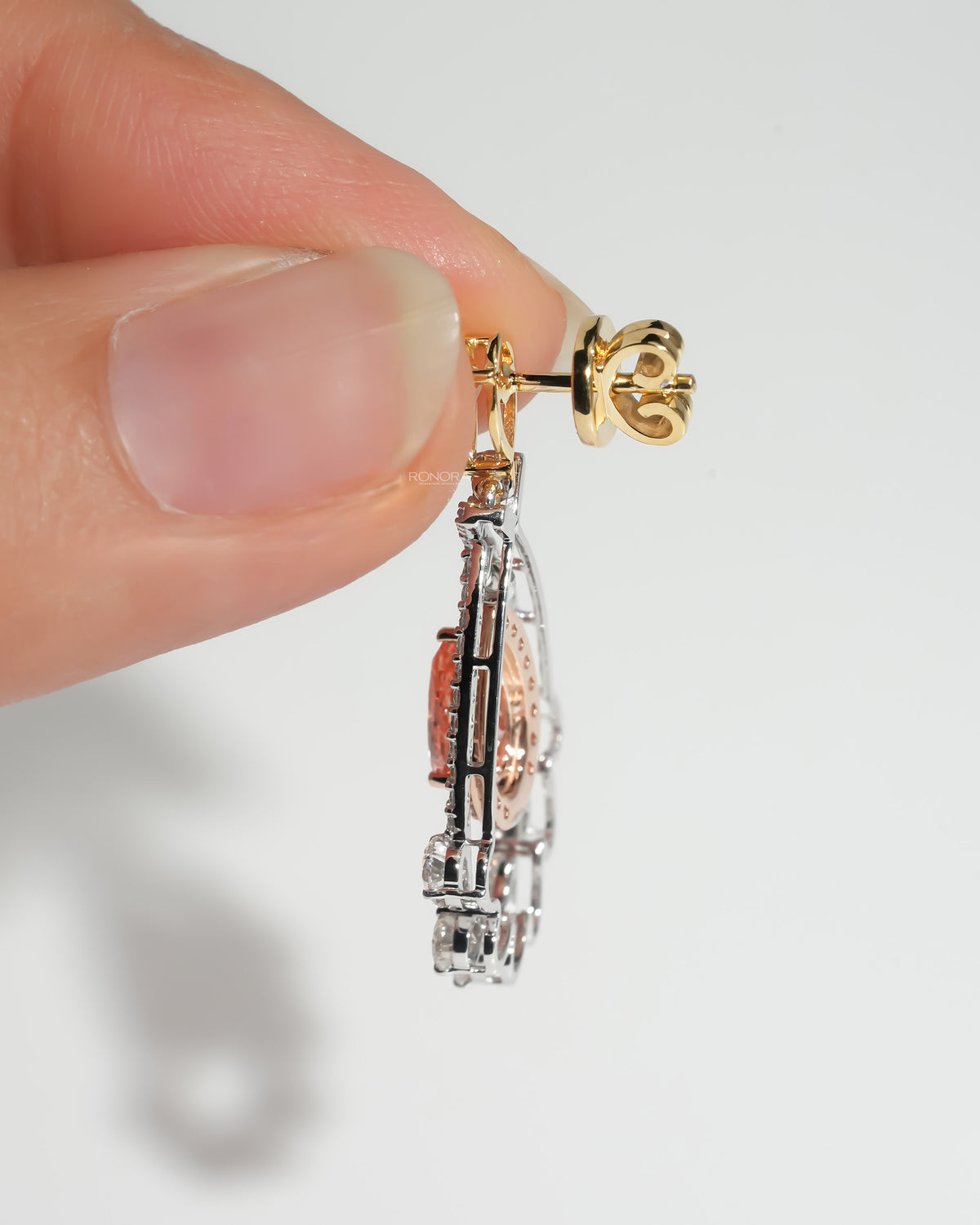 Side view of pink pear lab grown diamond drop earrings held in fingers, yellow gold post and open white diamond frame
