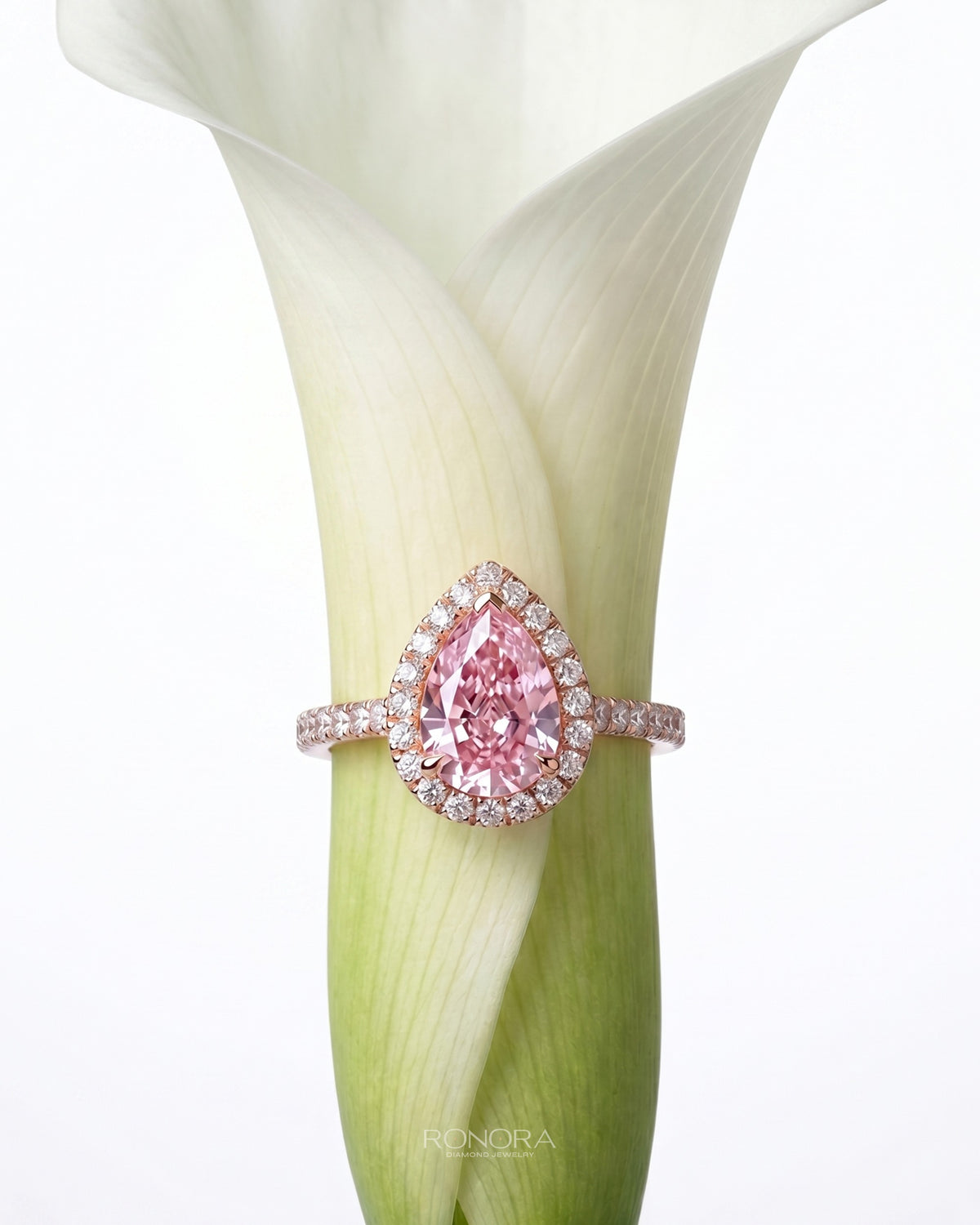 Pink pear moissanite halo ring in rose gold with a pave band, standing inside a white calla lily