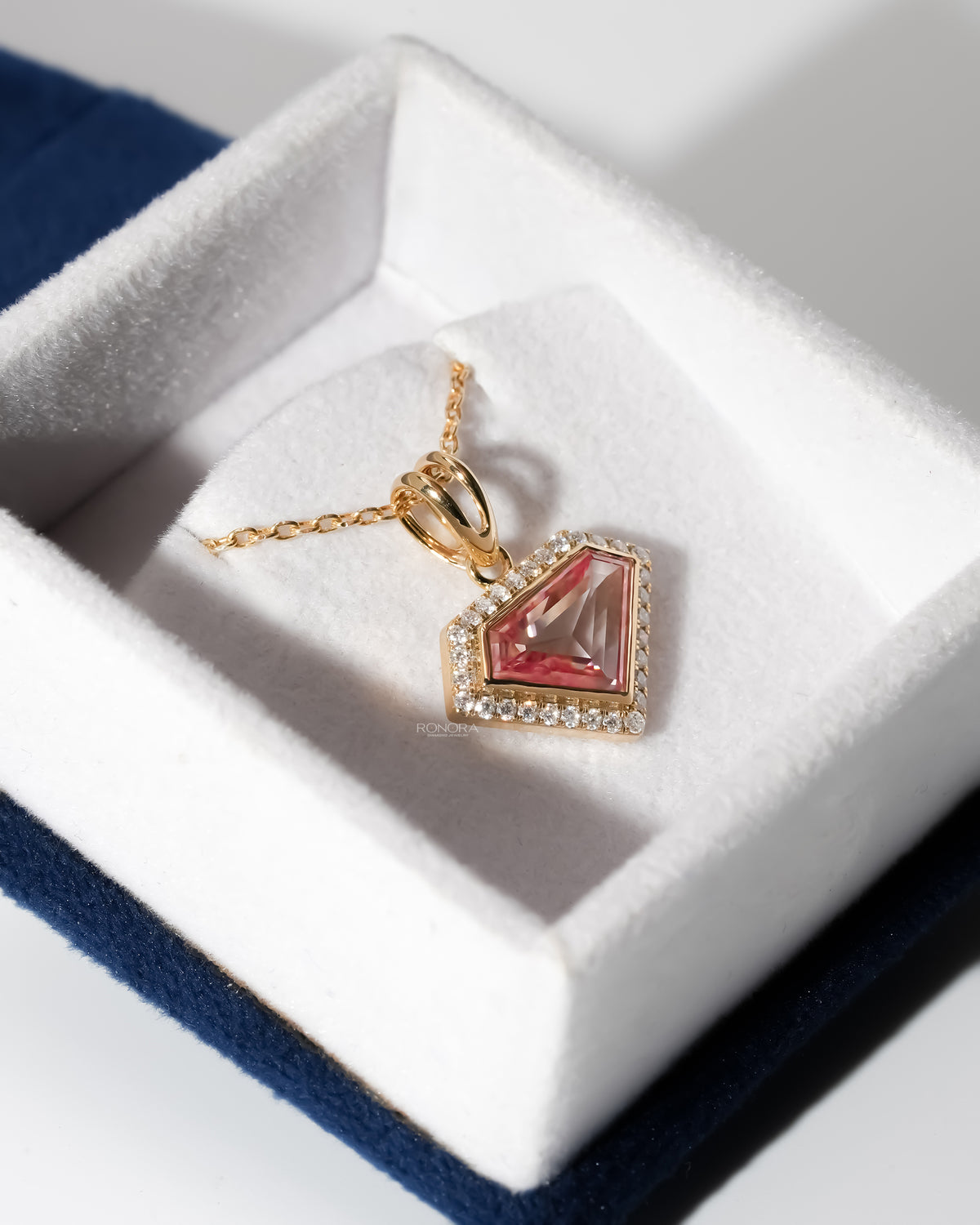 Pink shield cut lab grown diamond necklace in yellow gold lying in a white velvet jewelry box with a blue lid