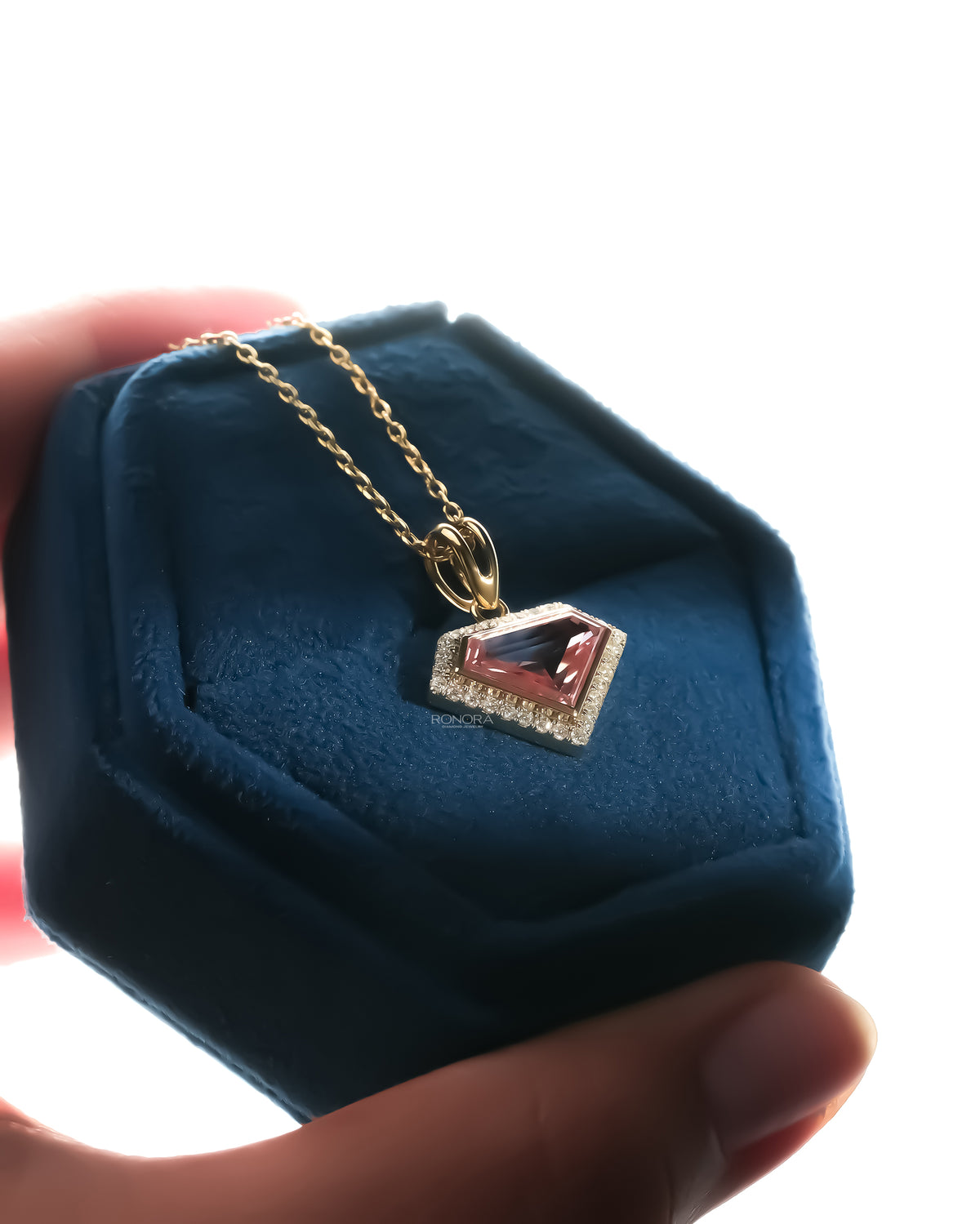Pink shield cut lab grown diamond necklace on a yellow gold chain in a blue velvet jewelry box held in hand