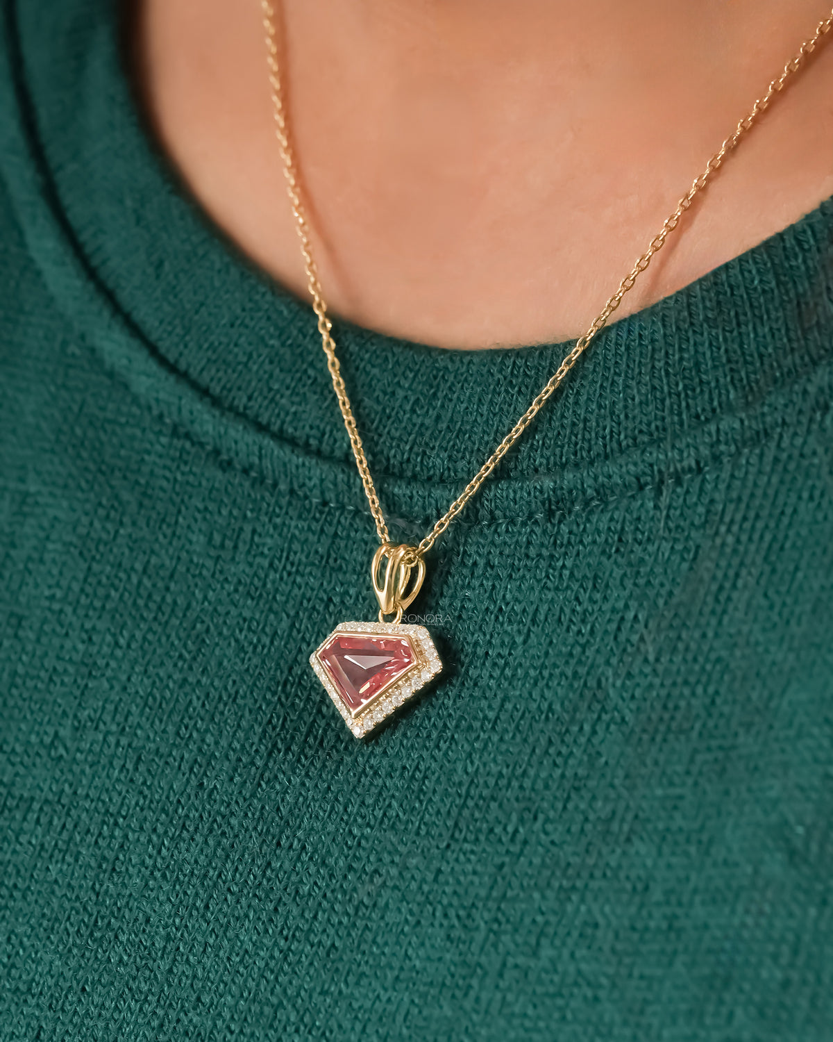Pink shield cut lab grown diamond necklace in yellow gold worn over a green knit sweater, angled close-up