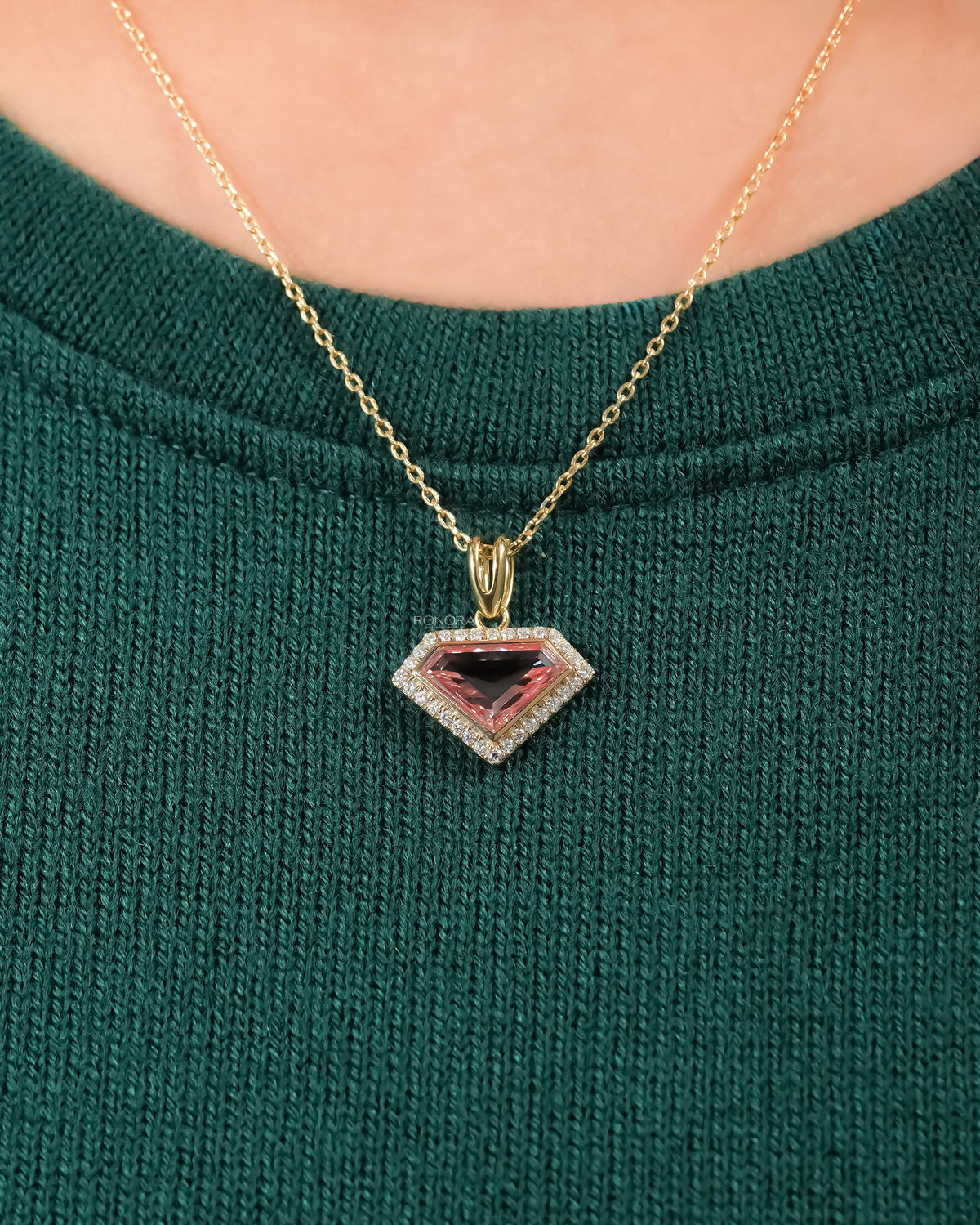Pink shield cut lab grown diamond necklace with a halo in yellow gold worn on a green knit sweater, front view