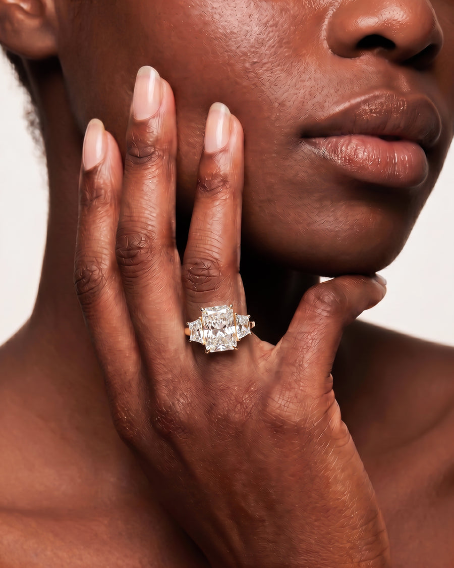 Woman with hand at her cheek wearing a radiant cut lab grown diamond three stone ring in yellow gold