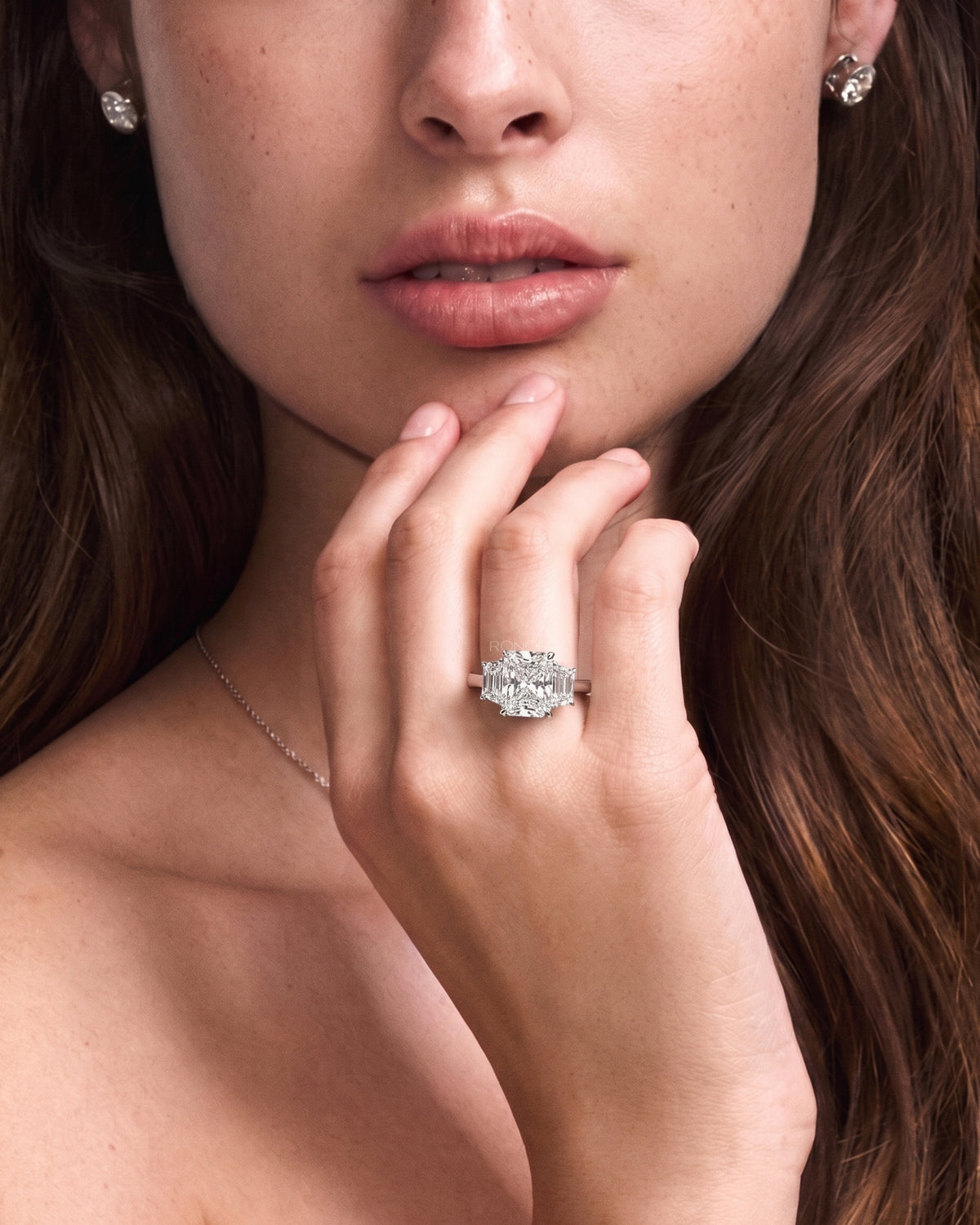 Model wearing a radiant three stone lab grown diamond ring with trapezoid side stones, hand at her chin