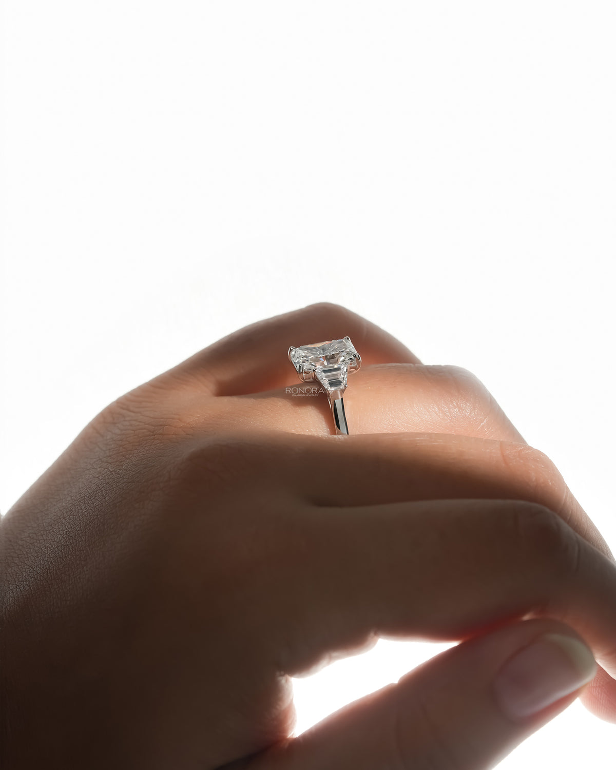 Side view of a radiant three stone lab grown diamond ring with trapezoid side stones worn on a finger