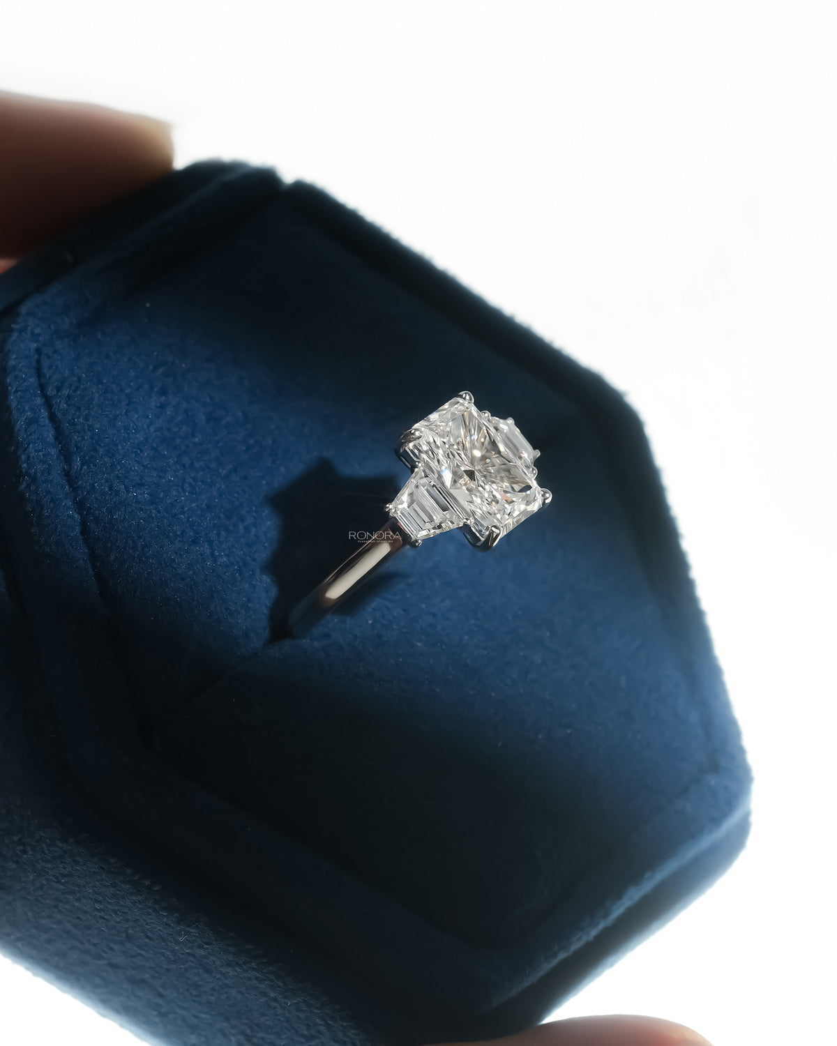 Angled view of a radiant three stone lab grown diamond ring with trapezoid side stones in a blue velvet box