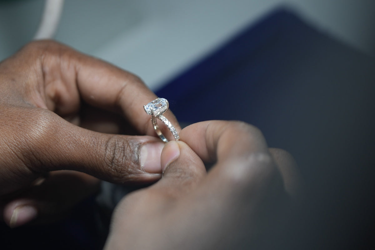 Hands hold up a finished white gold ring with an elongated center stone and a pave band for a close look