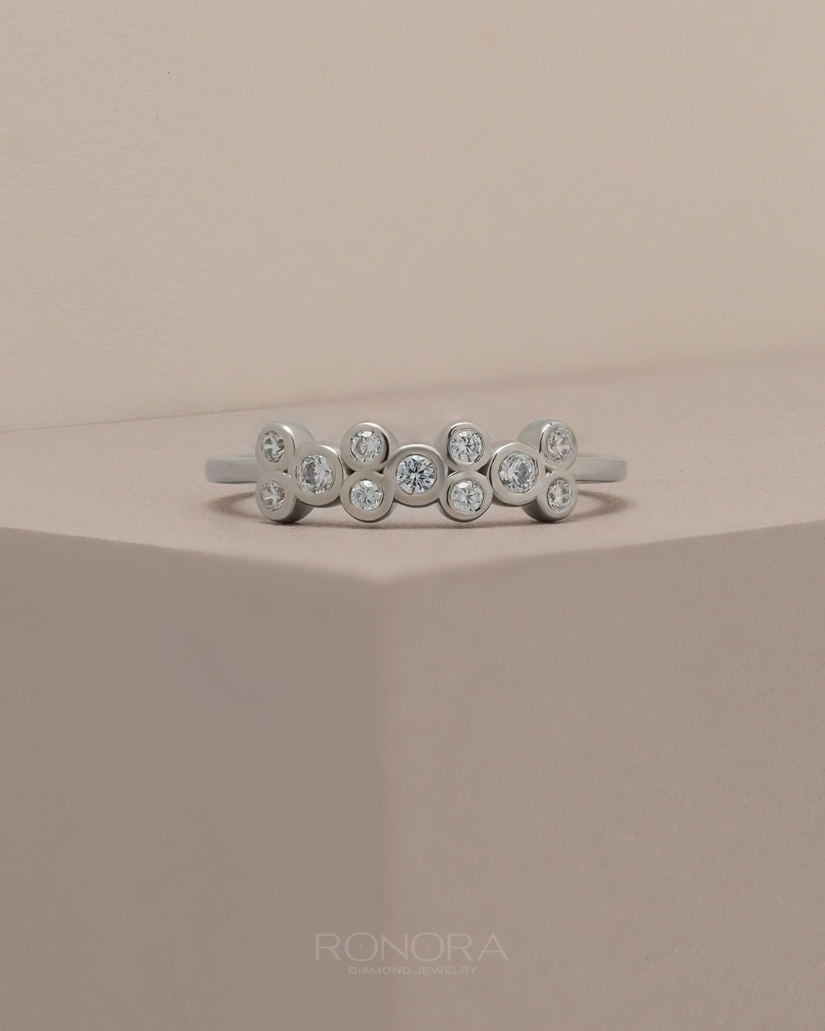 Stackable round bezel lab grown diamond band in white gold with bezel set round stones on a soft beige plinth