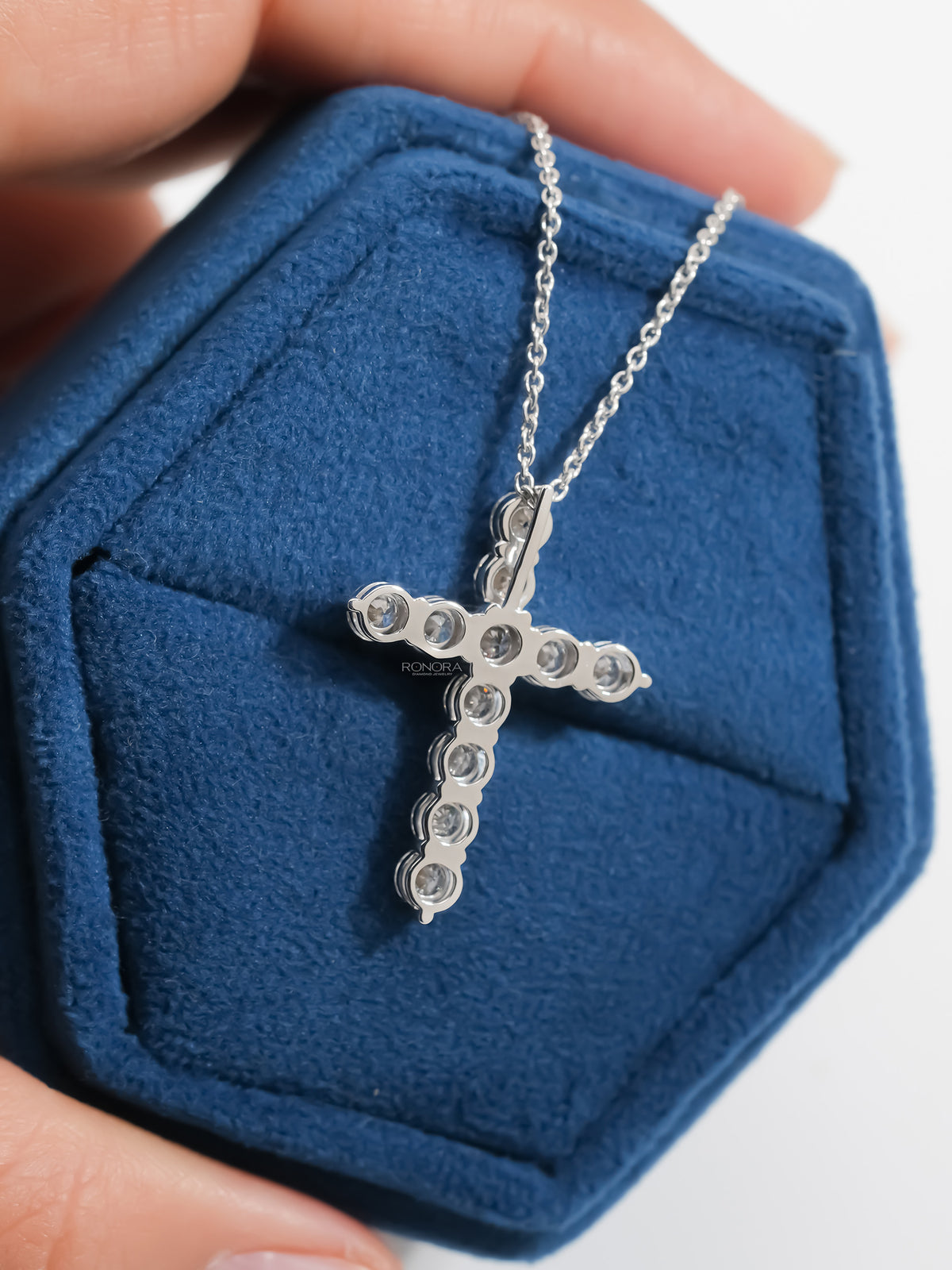 Back view of a round lab grown diamond cross necklace in a blue velvet jewelry box showing open prong settings