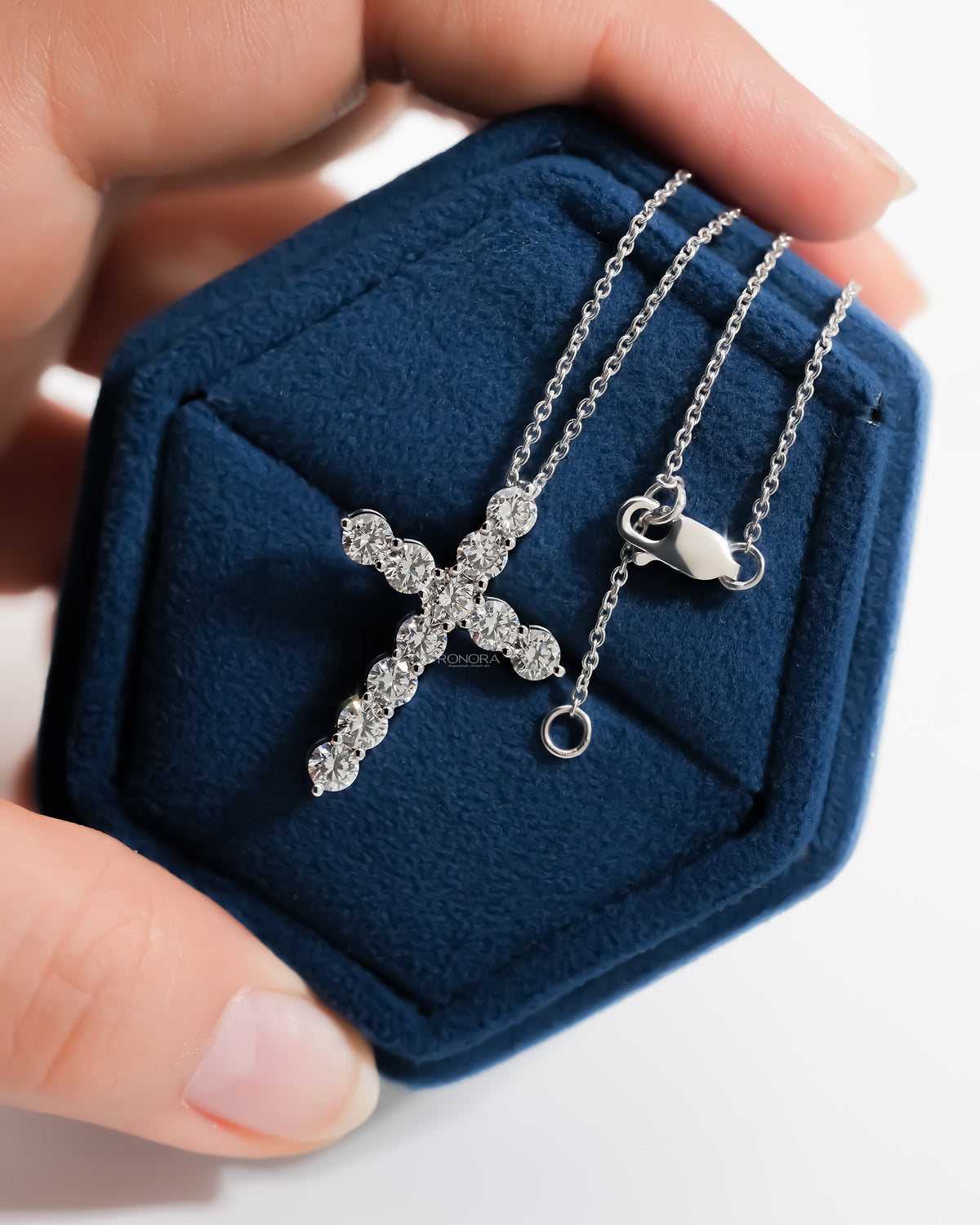 Round lab grown diamond cross necklace with chain and lobster clasp in a blue velvet hexagon jewelry box