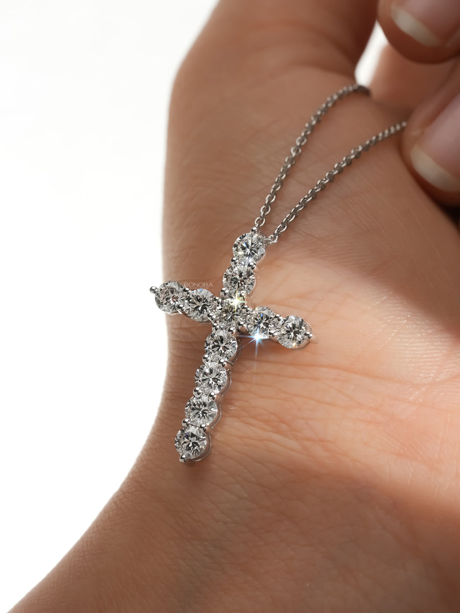 Round lab grown diamond cross necklace in white metal resting on the palm of a hand, close-up with bright sparkle