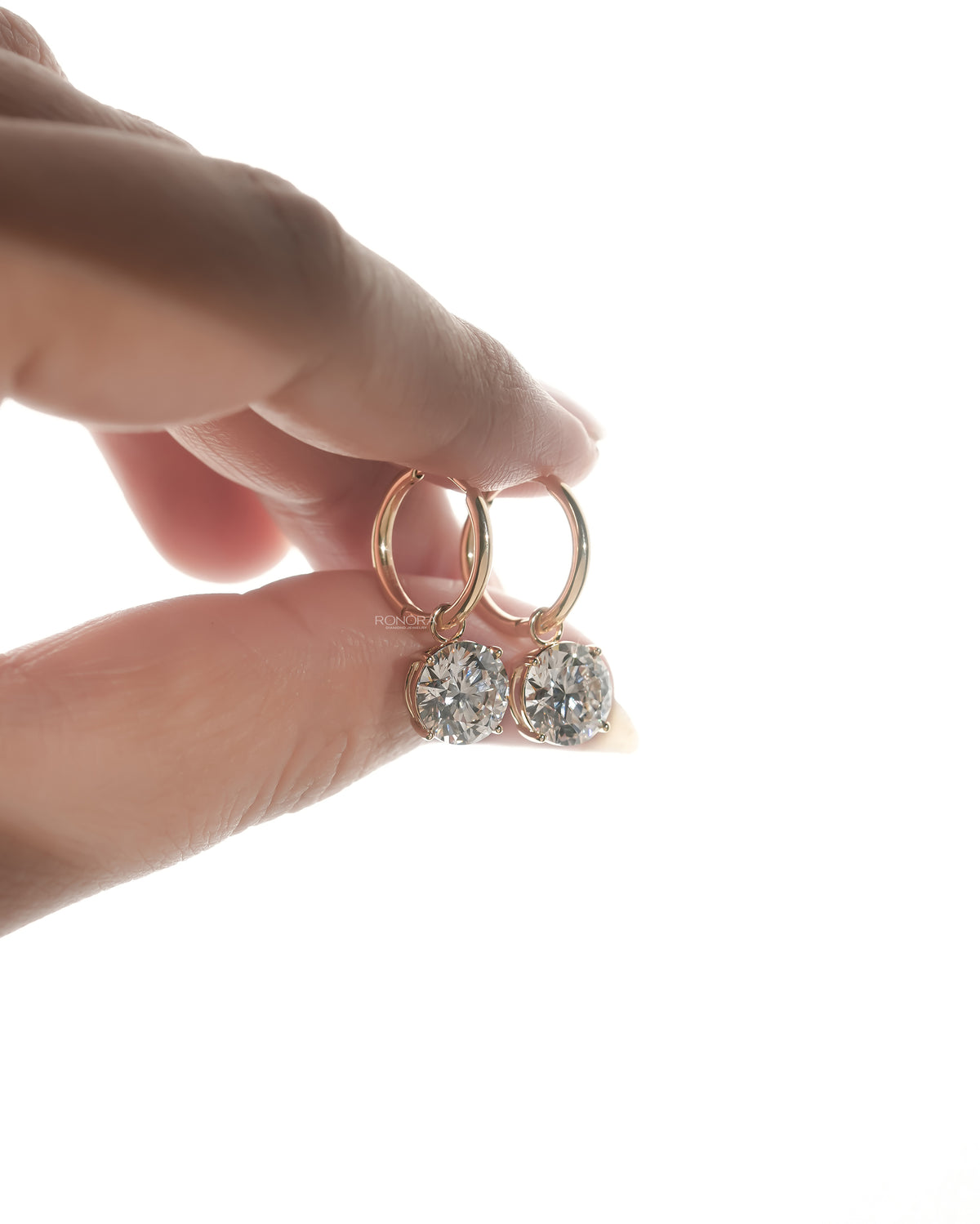 Side angle of lab grown diamond huggie drop earrings with round solitaire drops held in fingertips