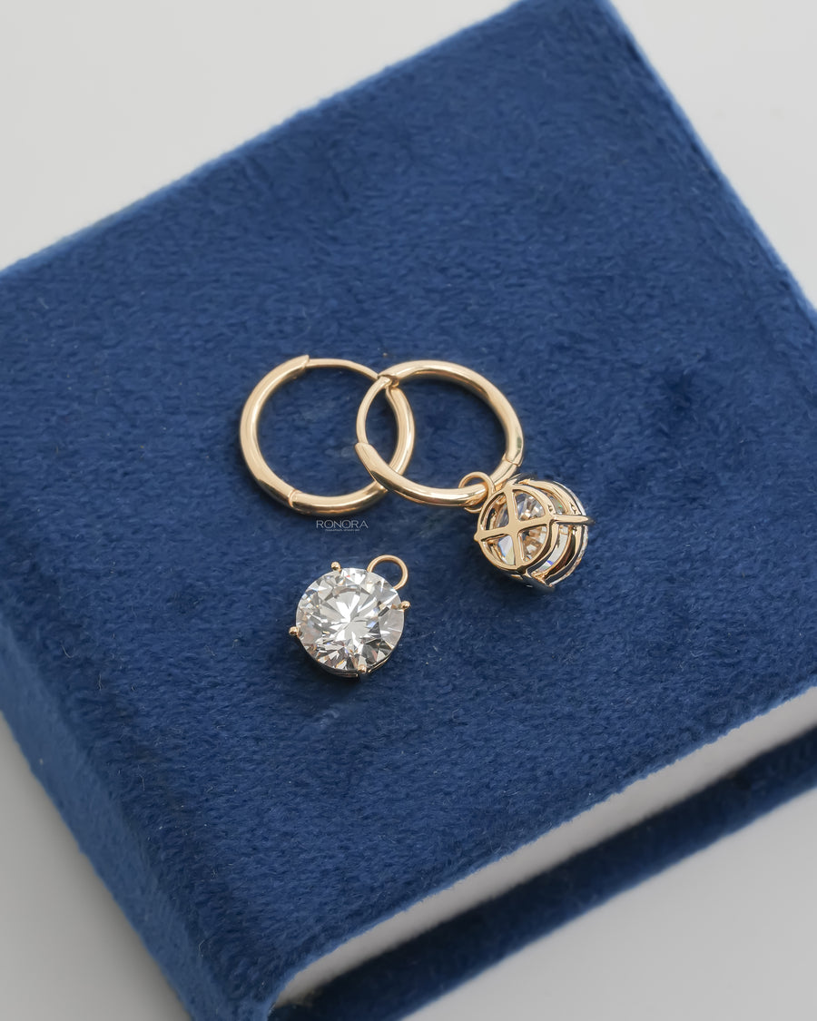 Detachable round lab grown diamond drop beside two yellow gold huggie hoops on blue velvet