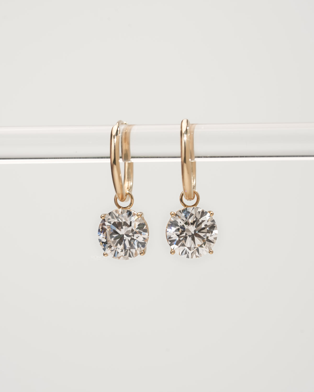 Round lab grown diamond huggie drop earrings in yellow gold hanging from a clear bar, front view