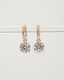 Round lab grown diamond huggie drop earrings in yellow gold hanging from a clear bar, front view