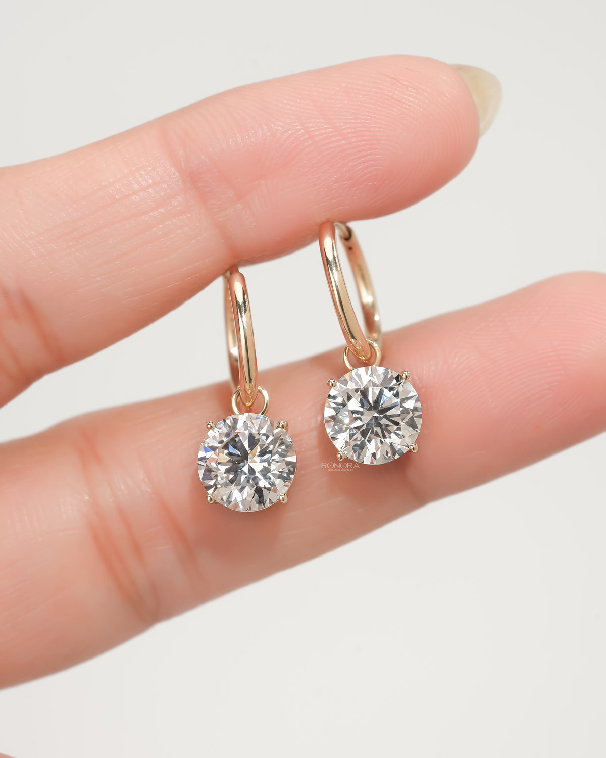 Round lab grown diamond huggie drop earrings in yellow gold held between two fingertips