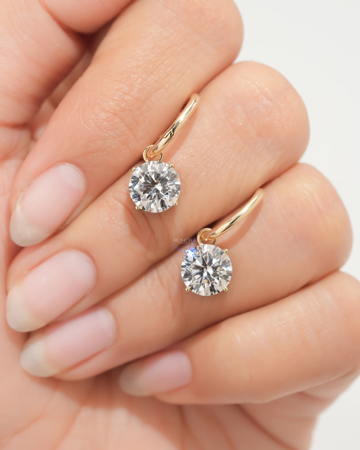 Pair of lab grown diamond huggie drop earrings with round solitaire drops held on a hand