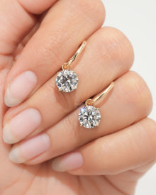 Pair of lab grown diamond huggie drop earrings with round solitaire drops held on a hand