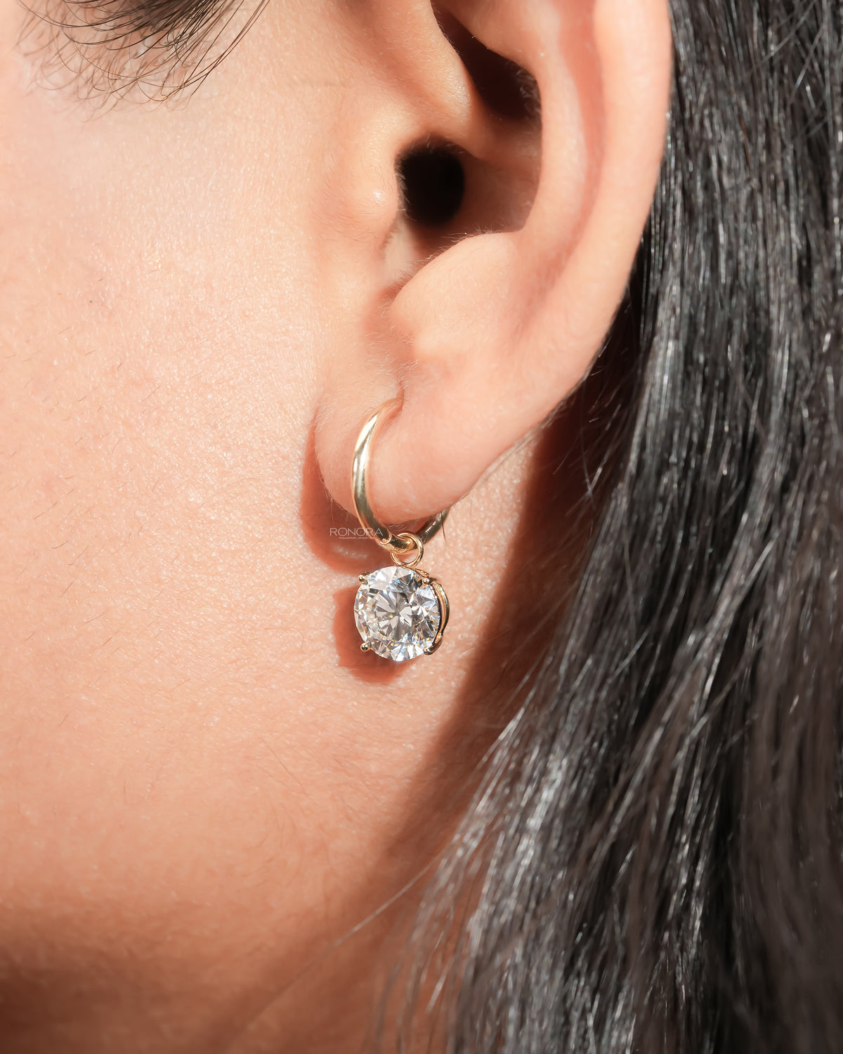 Close-up of a round lab grown diamond huggie drop earring with a yellow gold hoop worn on the ear