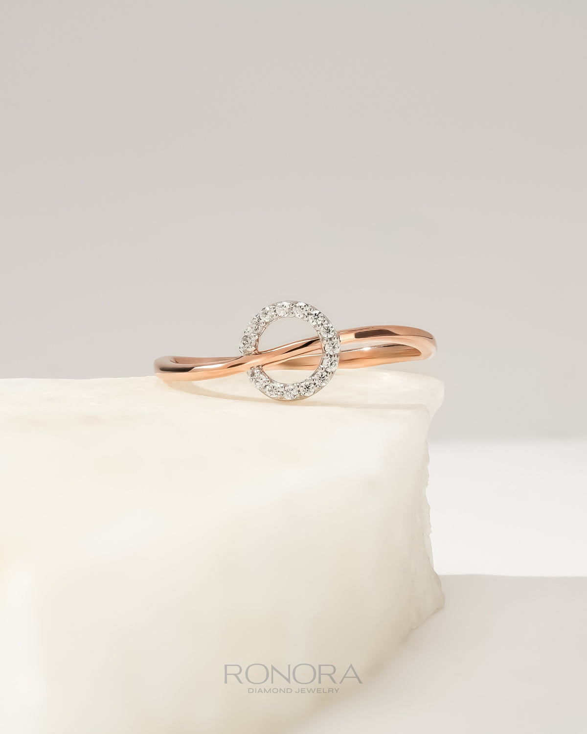 Round lab grown diamond open bypass ring in rose gold with a pave circle, resting on a white stone block