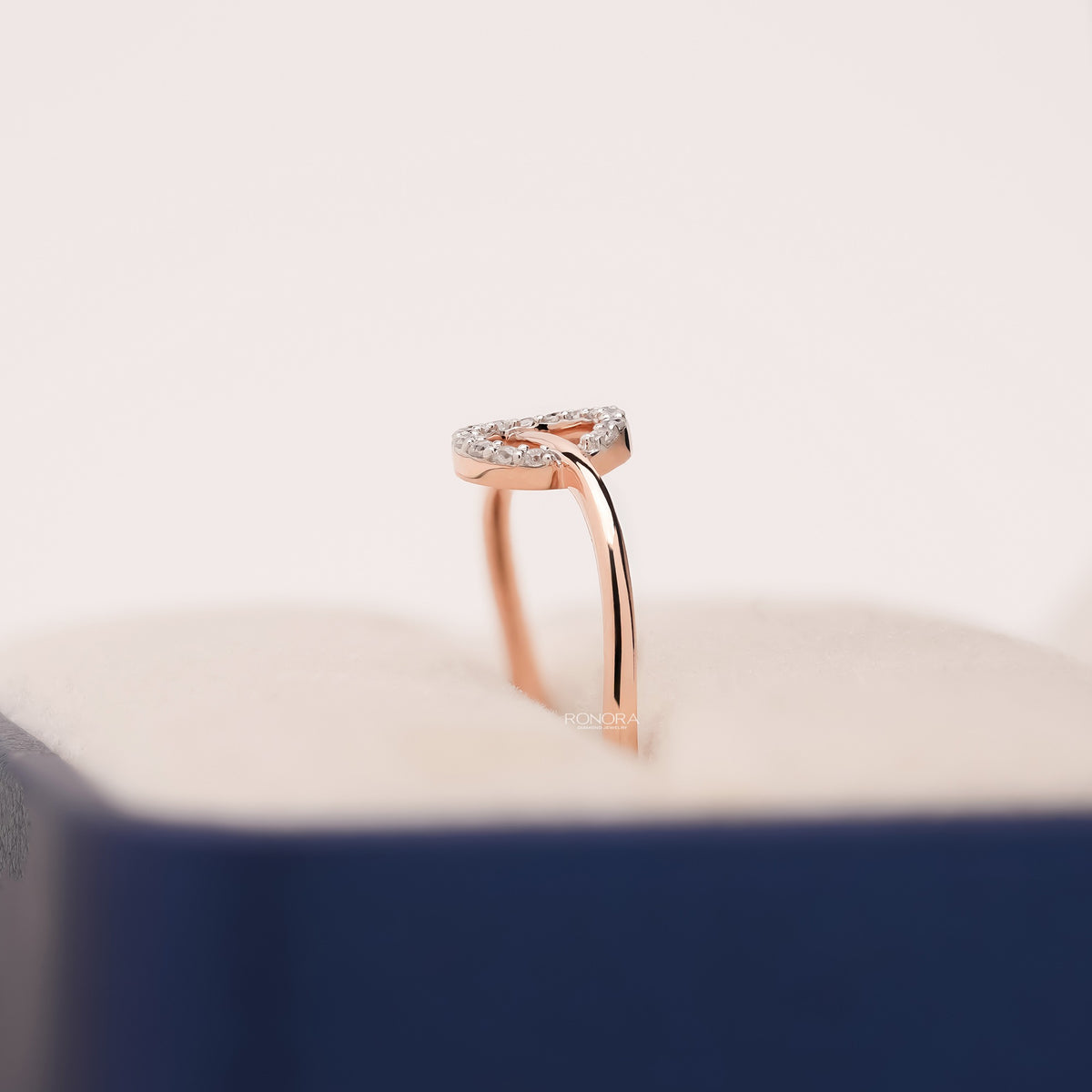 Side view of a rose gold round lab grown diamond open bypass ring with a pave circle in a blue ring box
