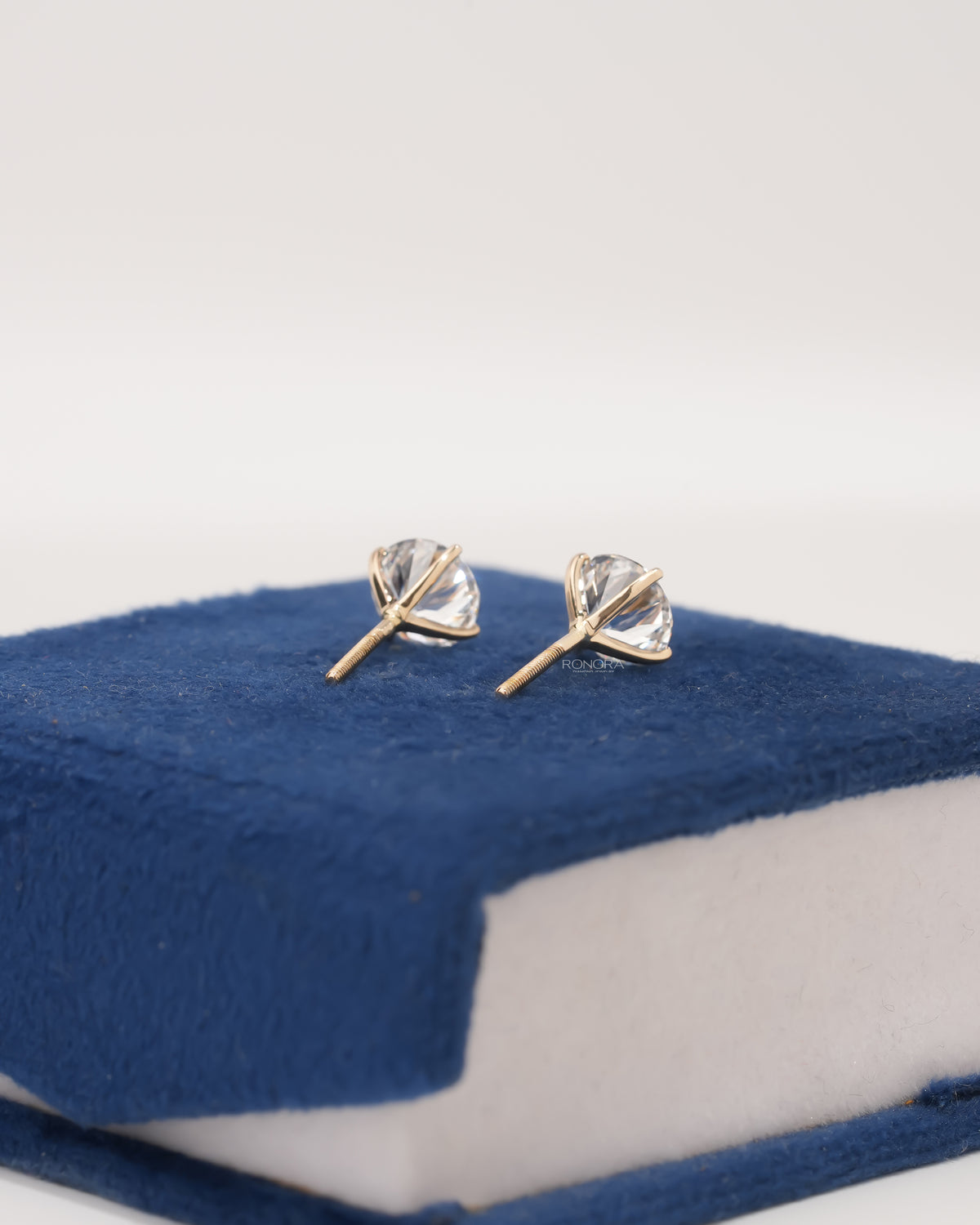 Back view of round lab grown diamond stud earrings with screw backs and yellow gold prongs on blue velvet