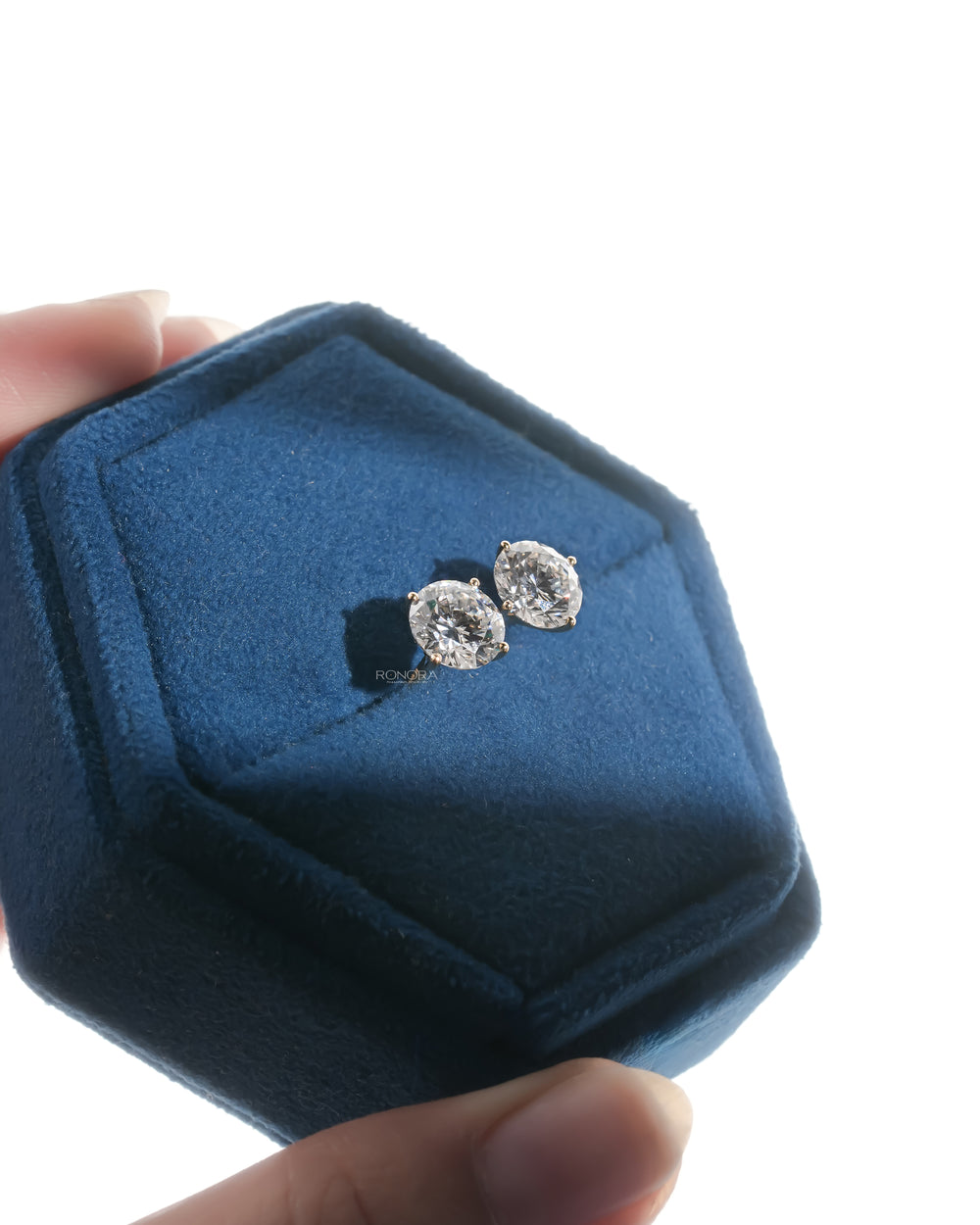 Tilted view of round lab grown diamond stud earrings inside a blue velvet jewelry box held in hand
