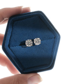 Round lab grown diamond stud earrings in four prong yellow gold shown in a hexagonal blue velvet jewelry box