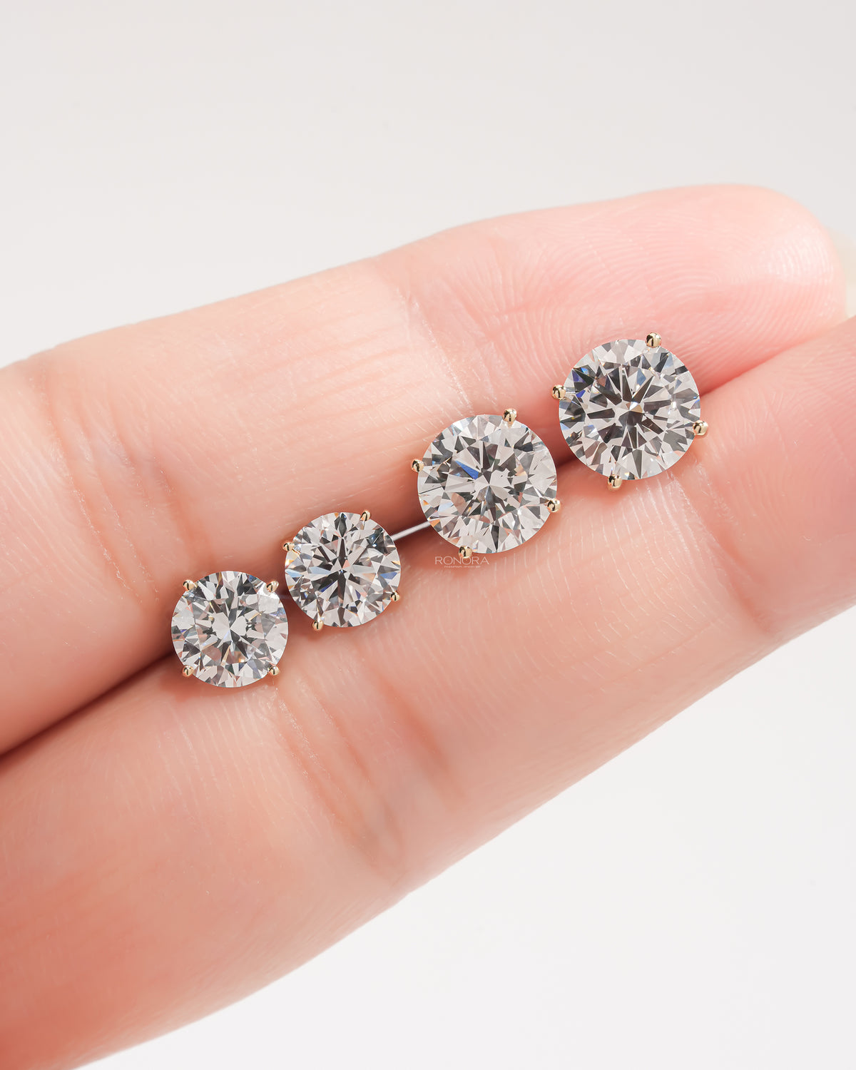 Four round lab grown diamond stud earrings in graduated sizes lined up on a fingertip for size comparison