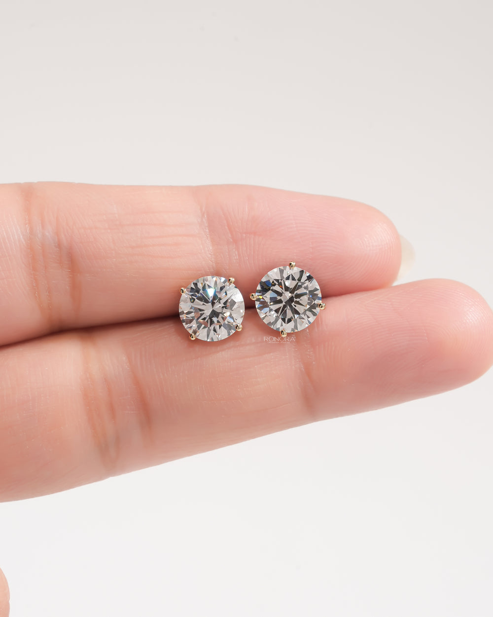Pair of round lab grown diamond stud earrings in four prong yellow gold settings resting on a fingertip