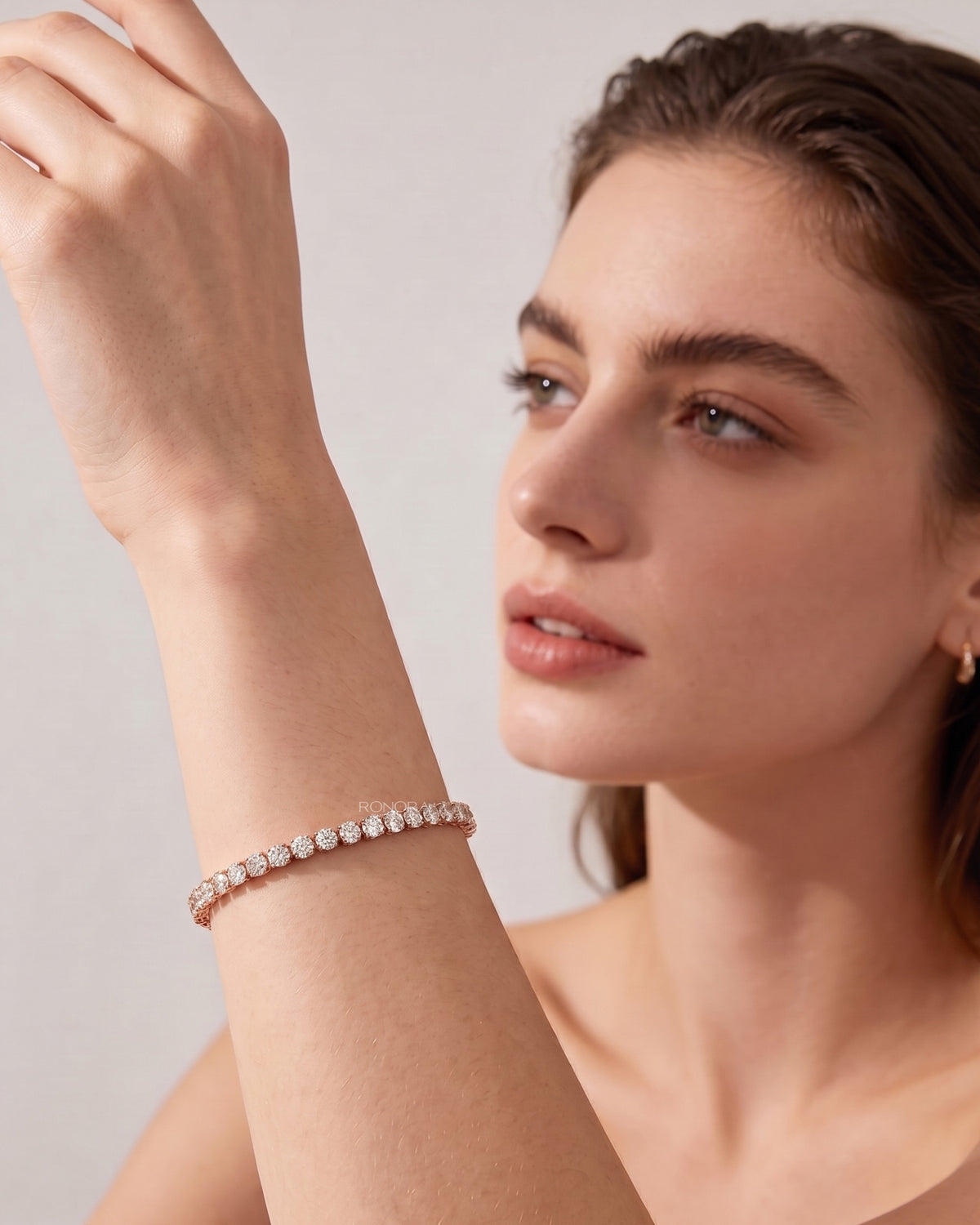 Model wearing a round lab grown diamond tennis bracelet in rose gold, arm raised, shown in side profile