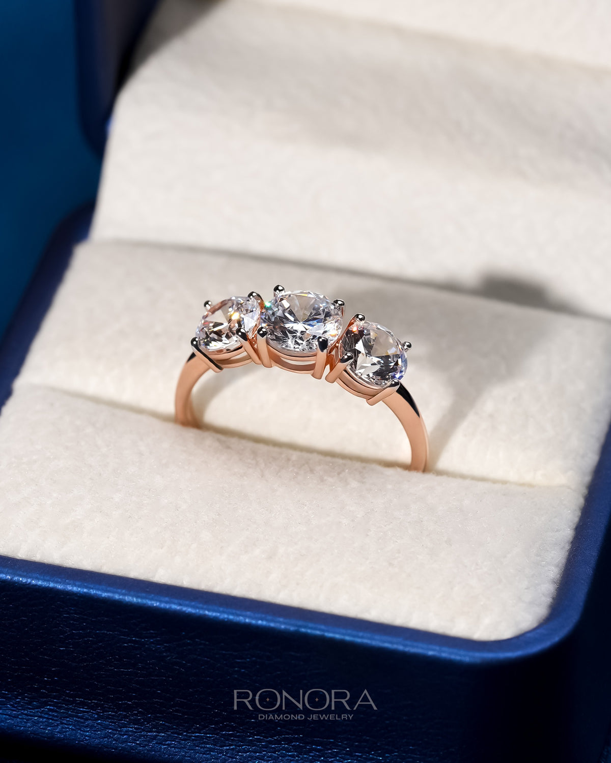 Round lab grown diamond three stone ring in rose gold with three round stones, angled view in a blue ring box