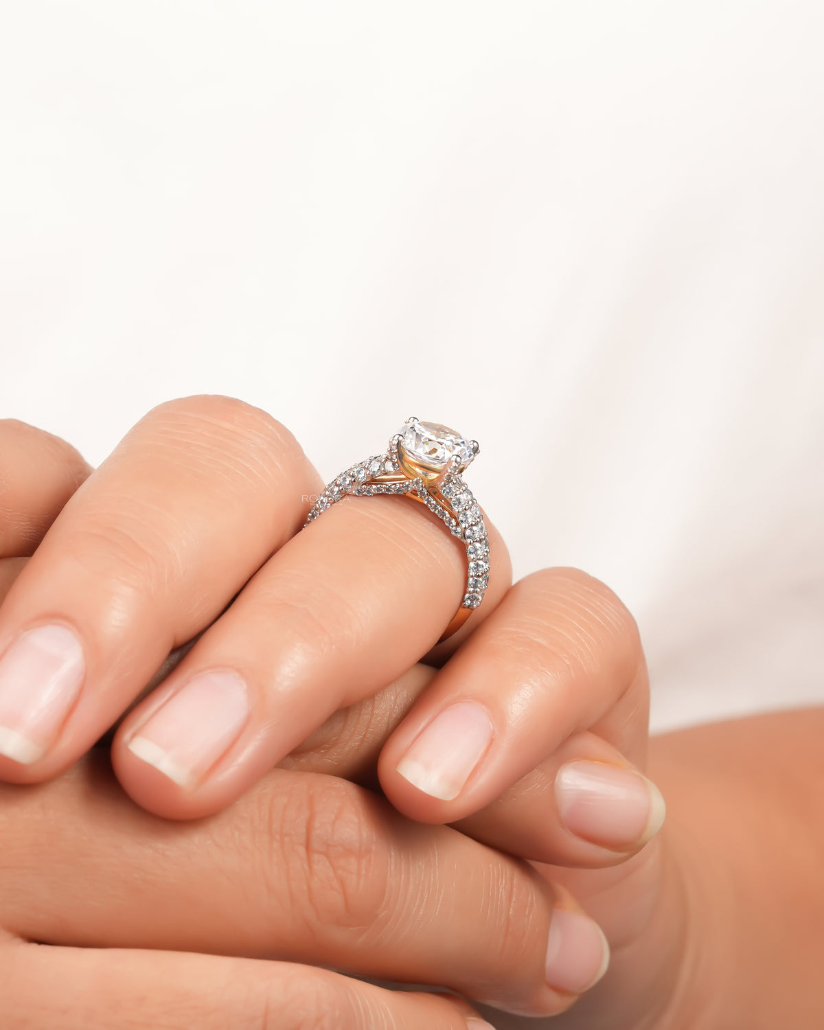 Angled view of a round moissanite solitaire engagement ring on a hand, pave band crossing under the stone