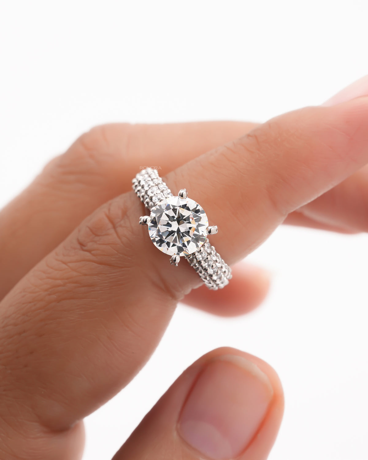 Close-up of a round moissanite engagement ring on a finger, six prong setting and a triple row pave band