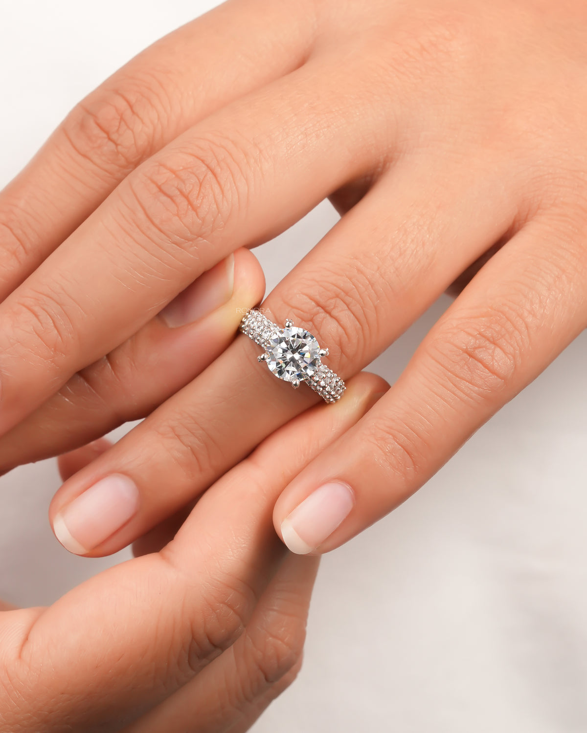 Hand wearing a round moissanite engagement ring with a six prong setting and a triple row pave band