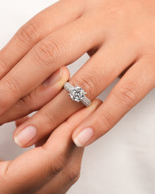 Hand wearing a round moissanite engagement ring with a six prong setting and a triple row pave band