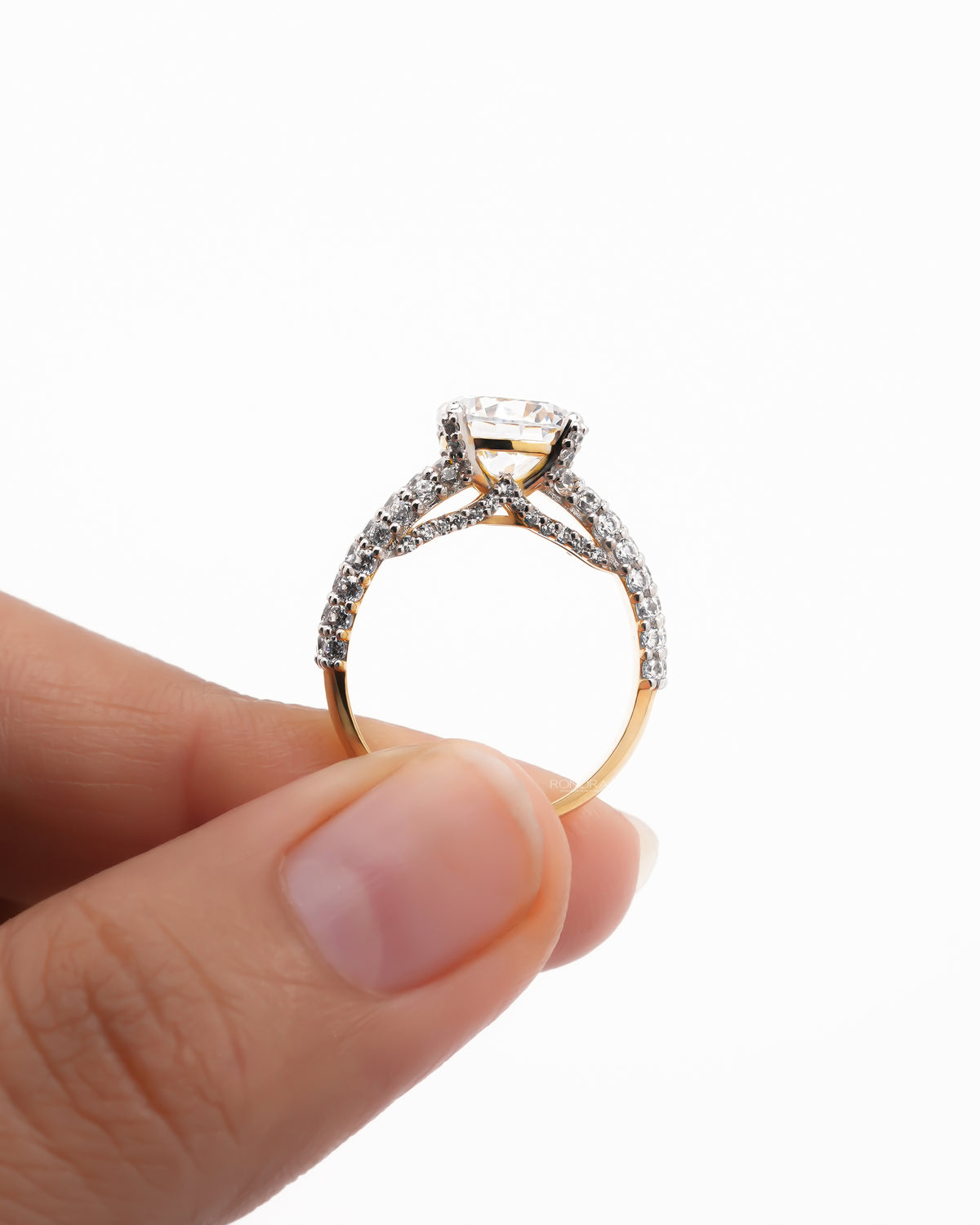 Profile of a round moissanite engagement ring held between fingers, pave arms crossing under the stone