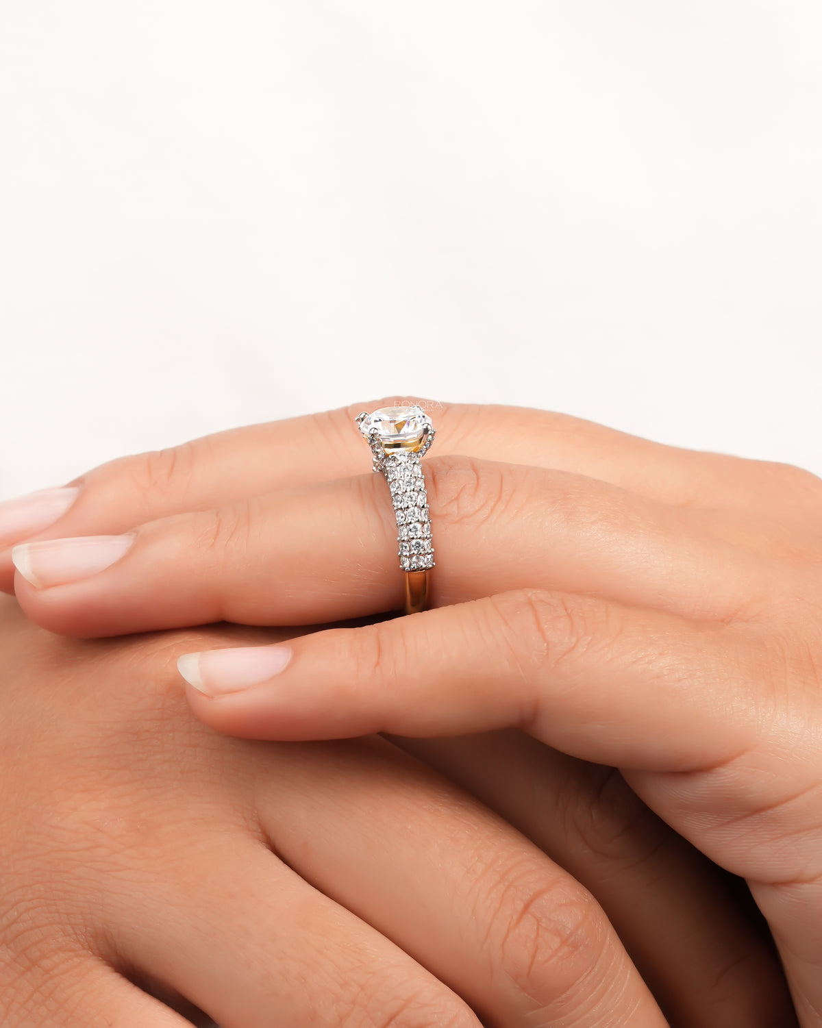 Side view of a round moissanite engagement ring on a finger, wide pave band with a yellow gold base