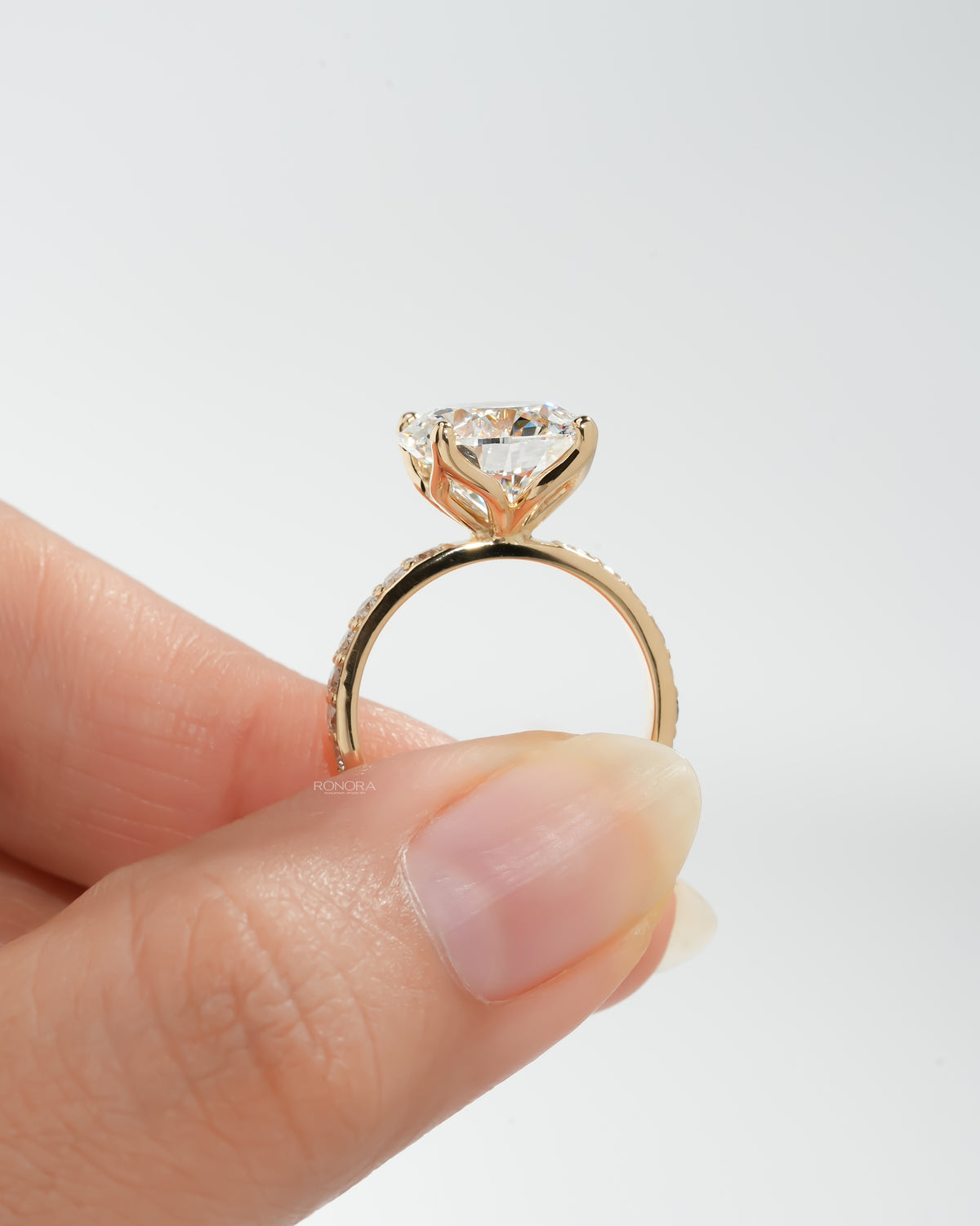 Round pave lab grown diamond engagement ring held in fingers, side view of the tulip prongs and pave gold band