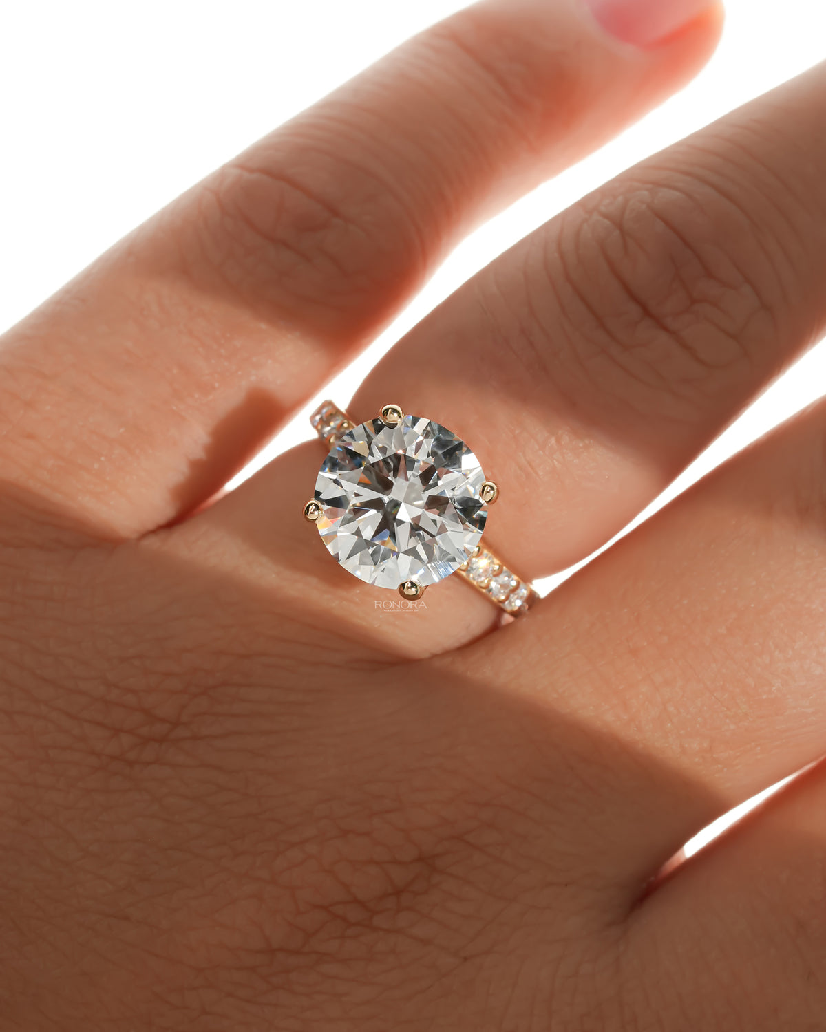 Round pave lab grown diamond engagement ring on a hand in warm light, front view with pave band