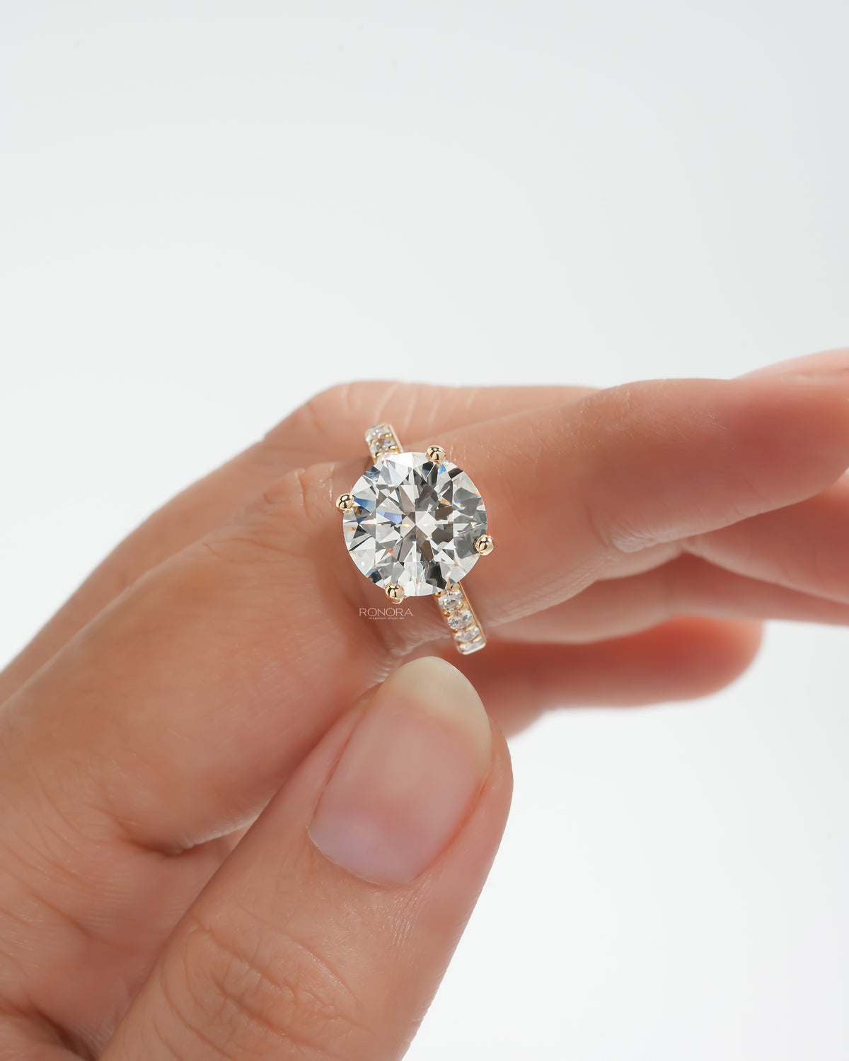 Round pave lab grown diamond engagement ring on a finger, front view of the round stone with pave band