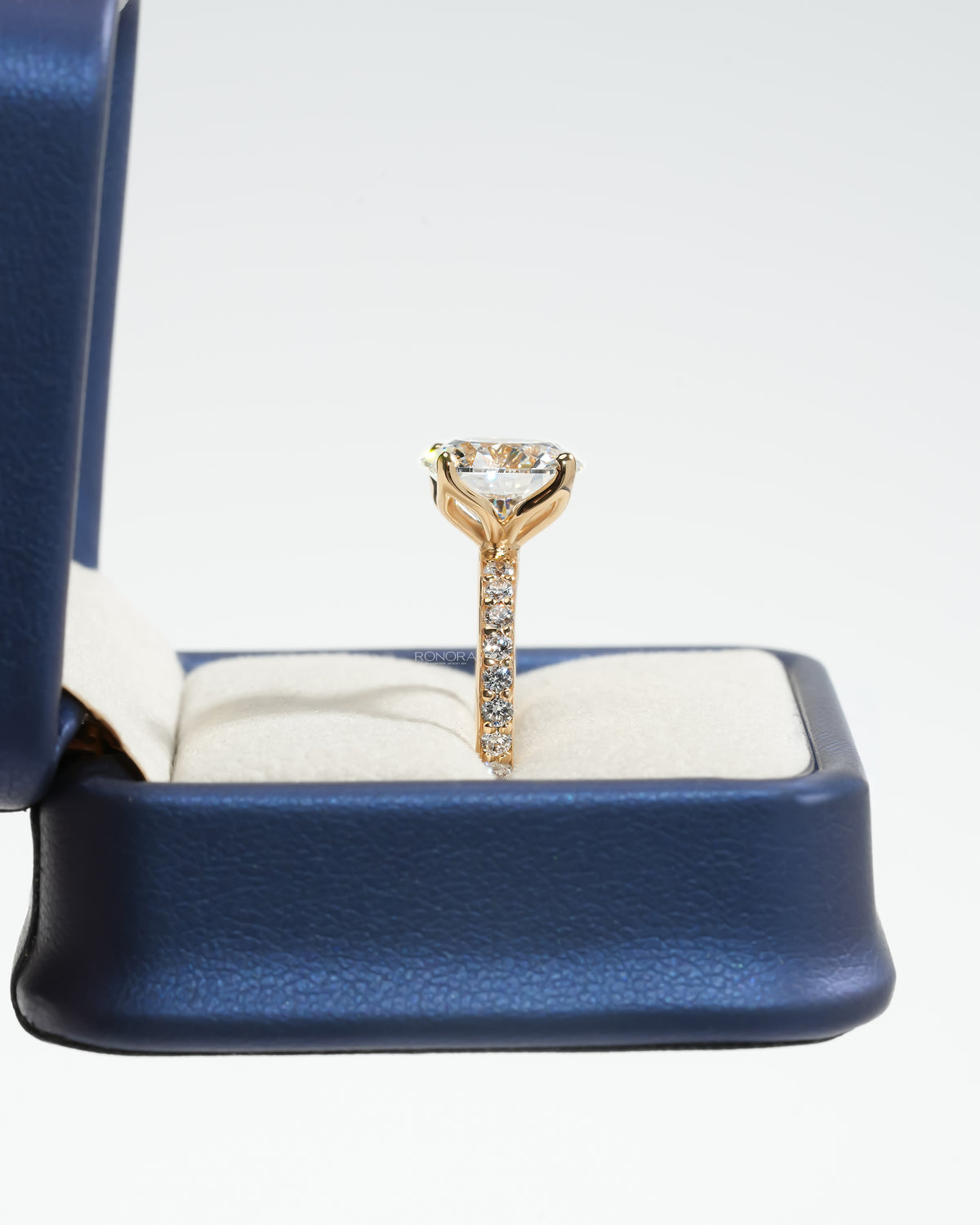 Side view of a round pave lab grown diamond engagement ring in a blue ring box showing the pave band