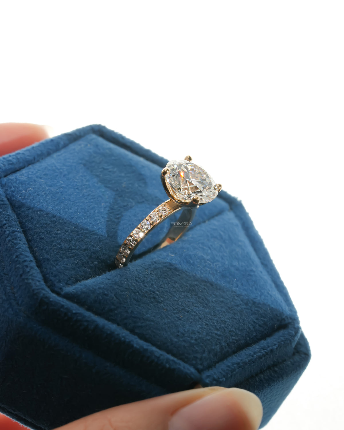Round pave lab grown diamond engagement ring in a blue velvet ring box, angled view of the pave band