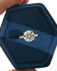 Round pave lab grown diamond engagement ring in a blue velvet ring box, top view with four prongs